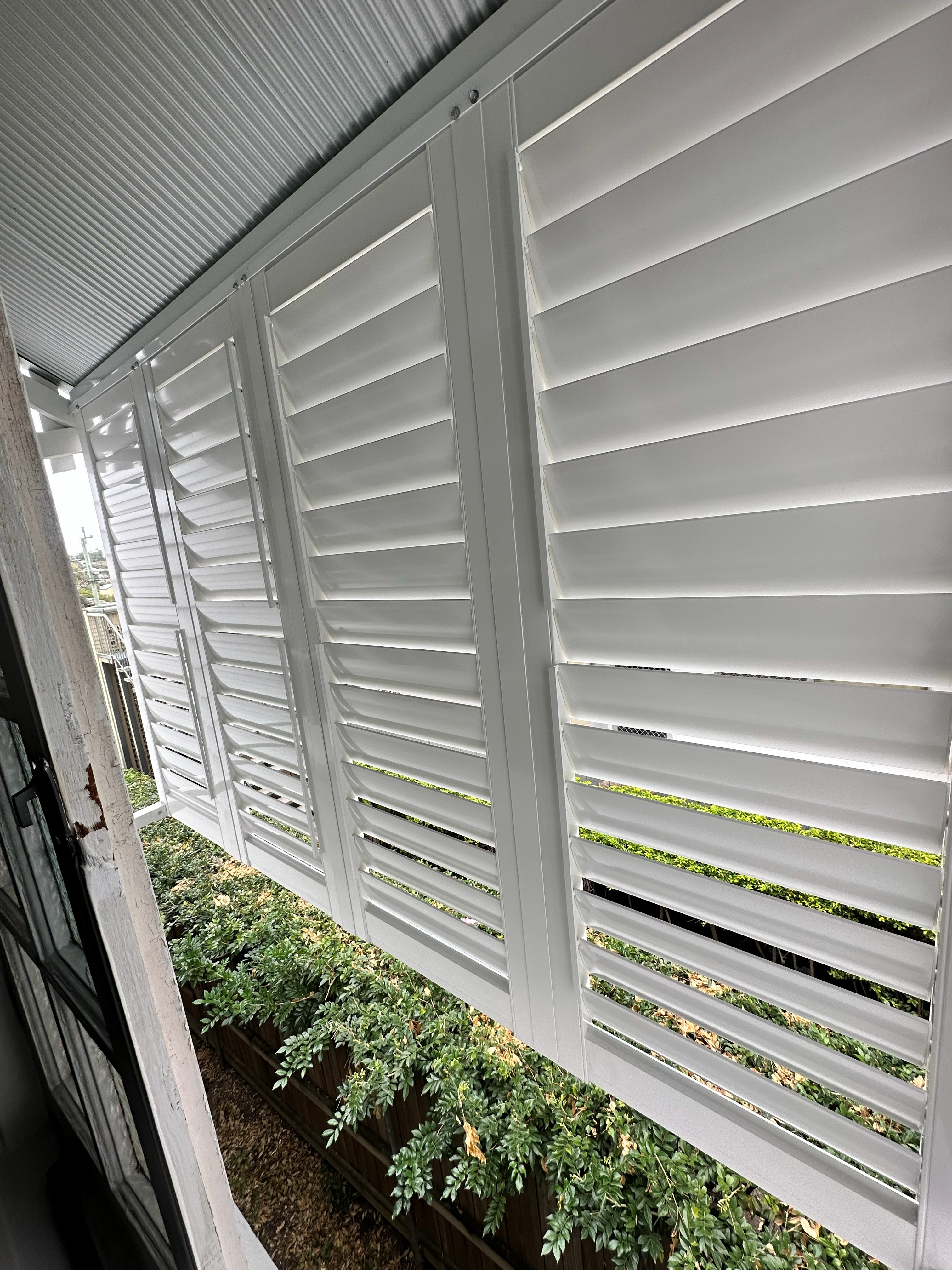 Black aluminium shutters fitted along a covered patio with brick pillars