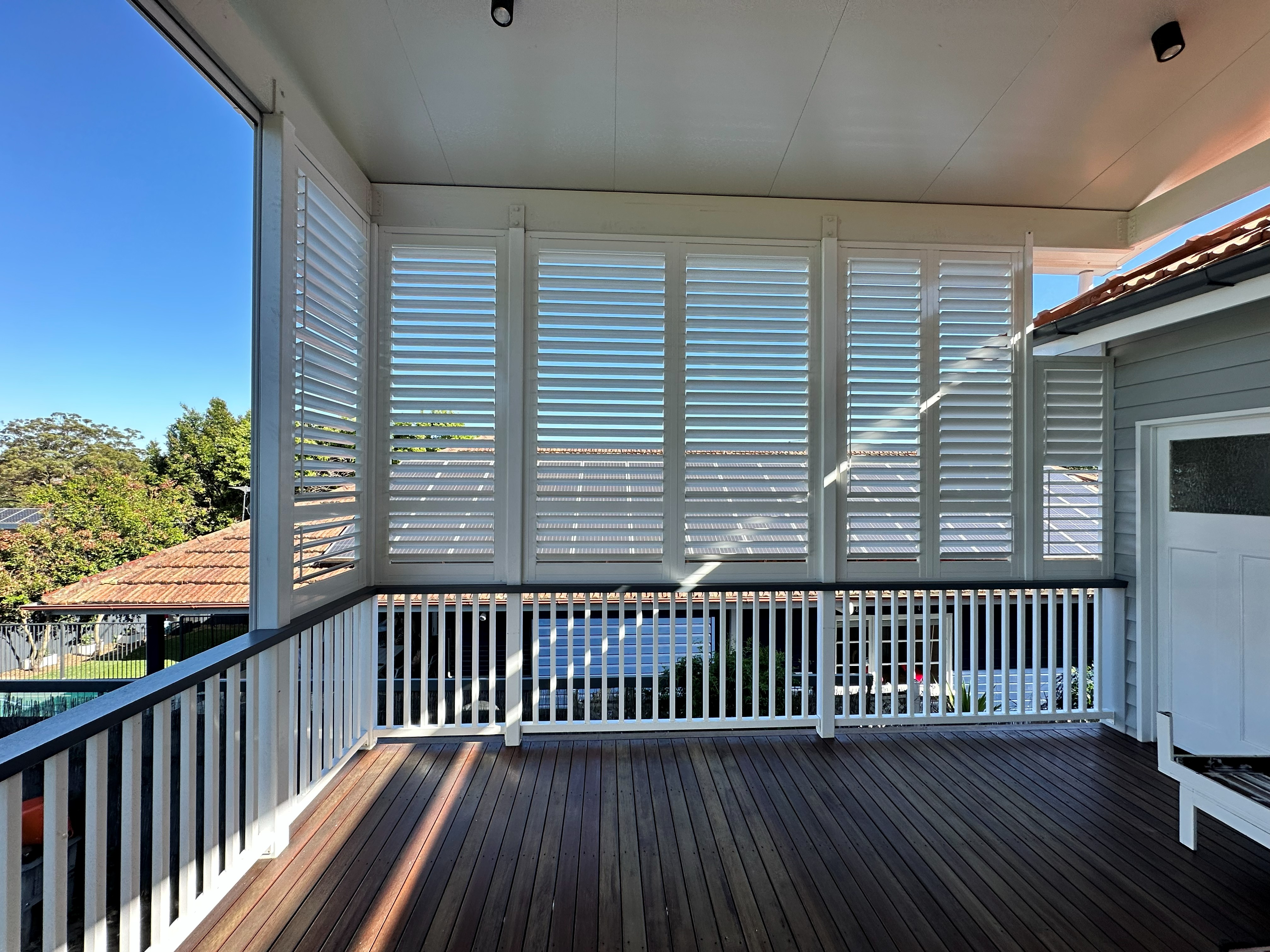 Charcoal aluminium shutters fitted to a covered deck overlooking a garden