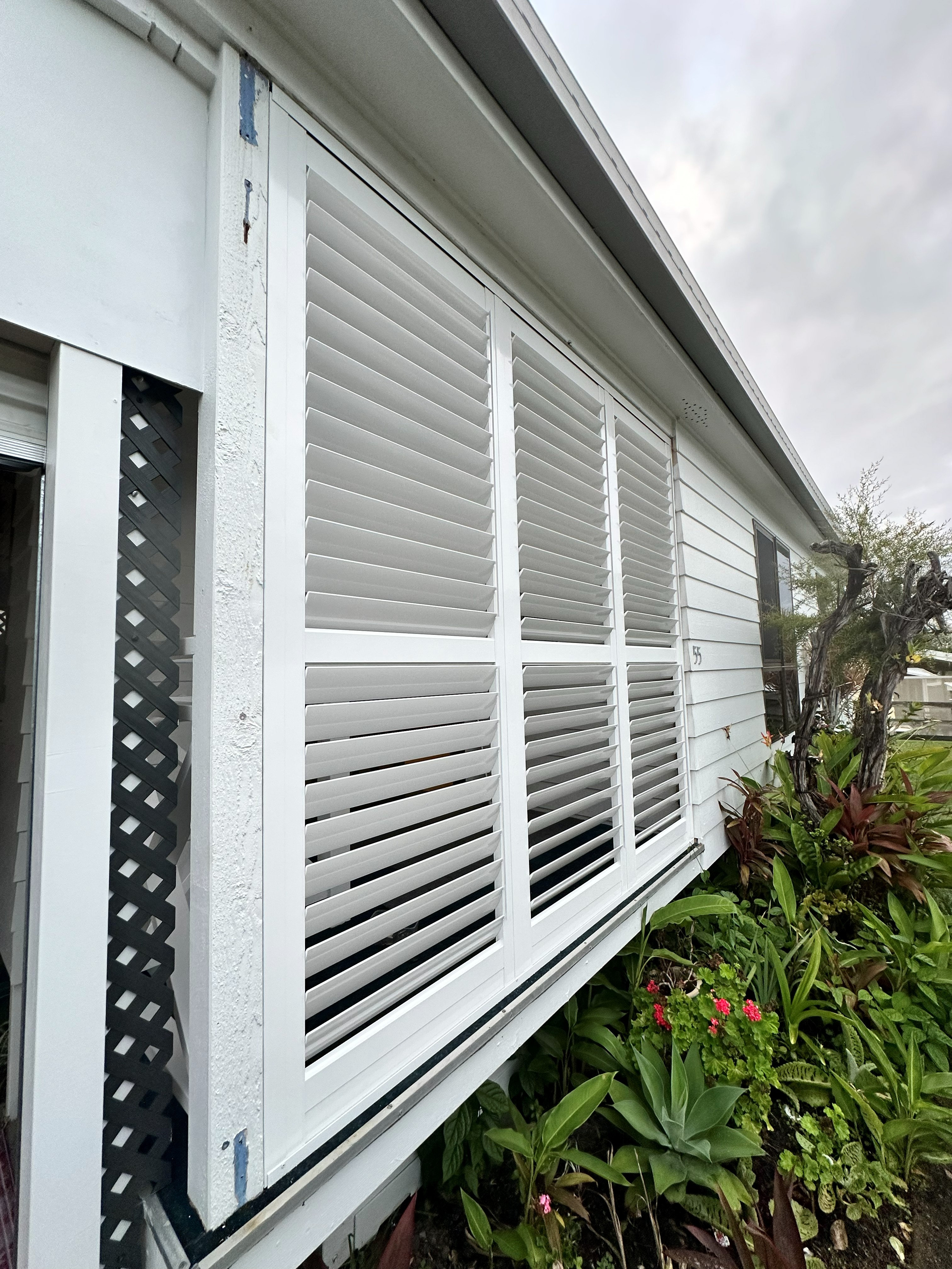 White aluminium shutters fitted over three windows on a weatherboard home