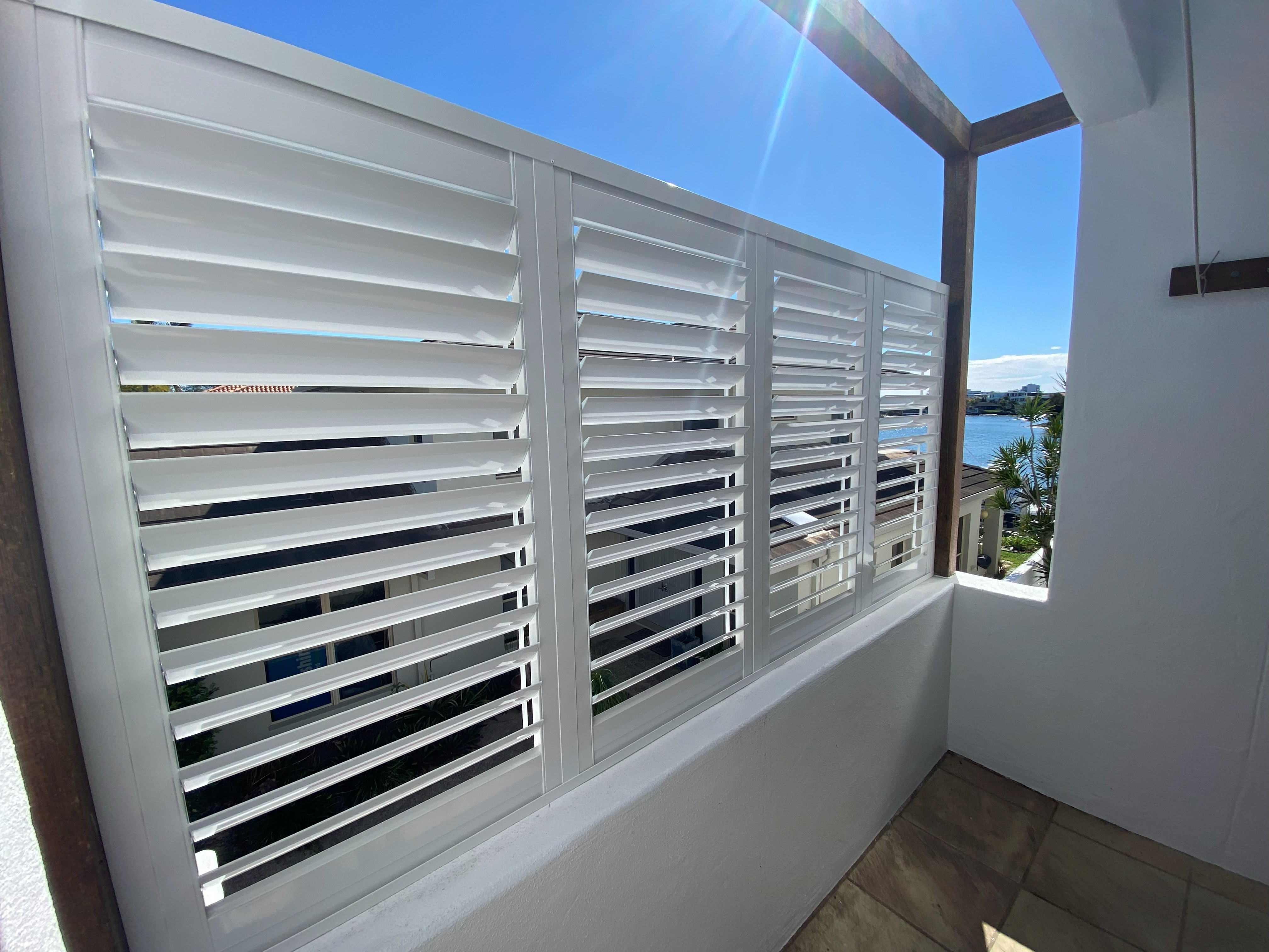 White aluminium shutters on a high-rise balcony overlooking the water