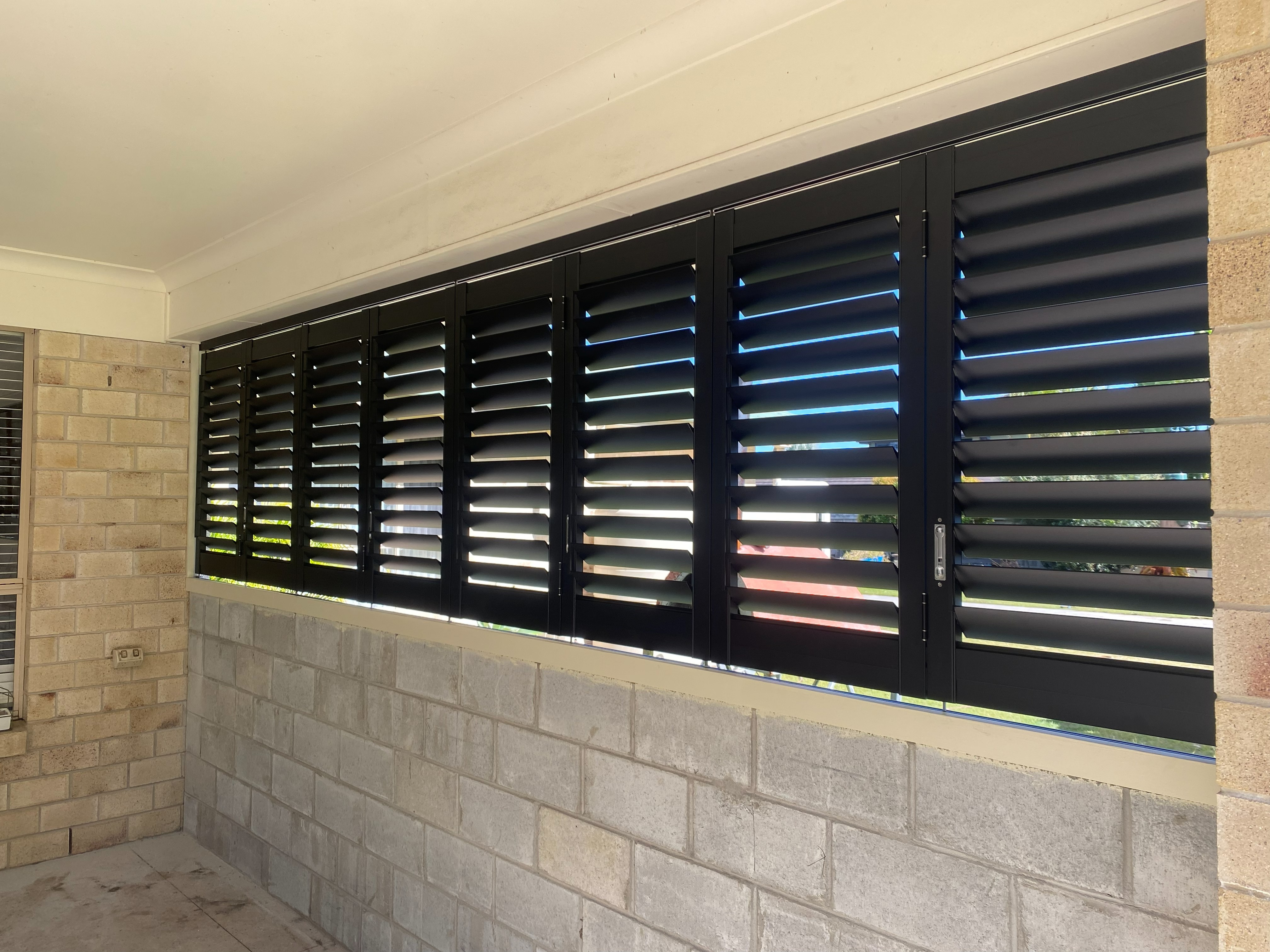 Black aluminium shutters fitted along a brick home patio