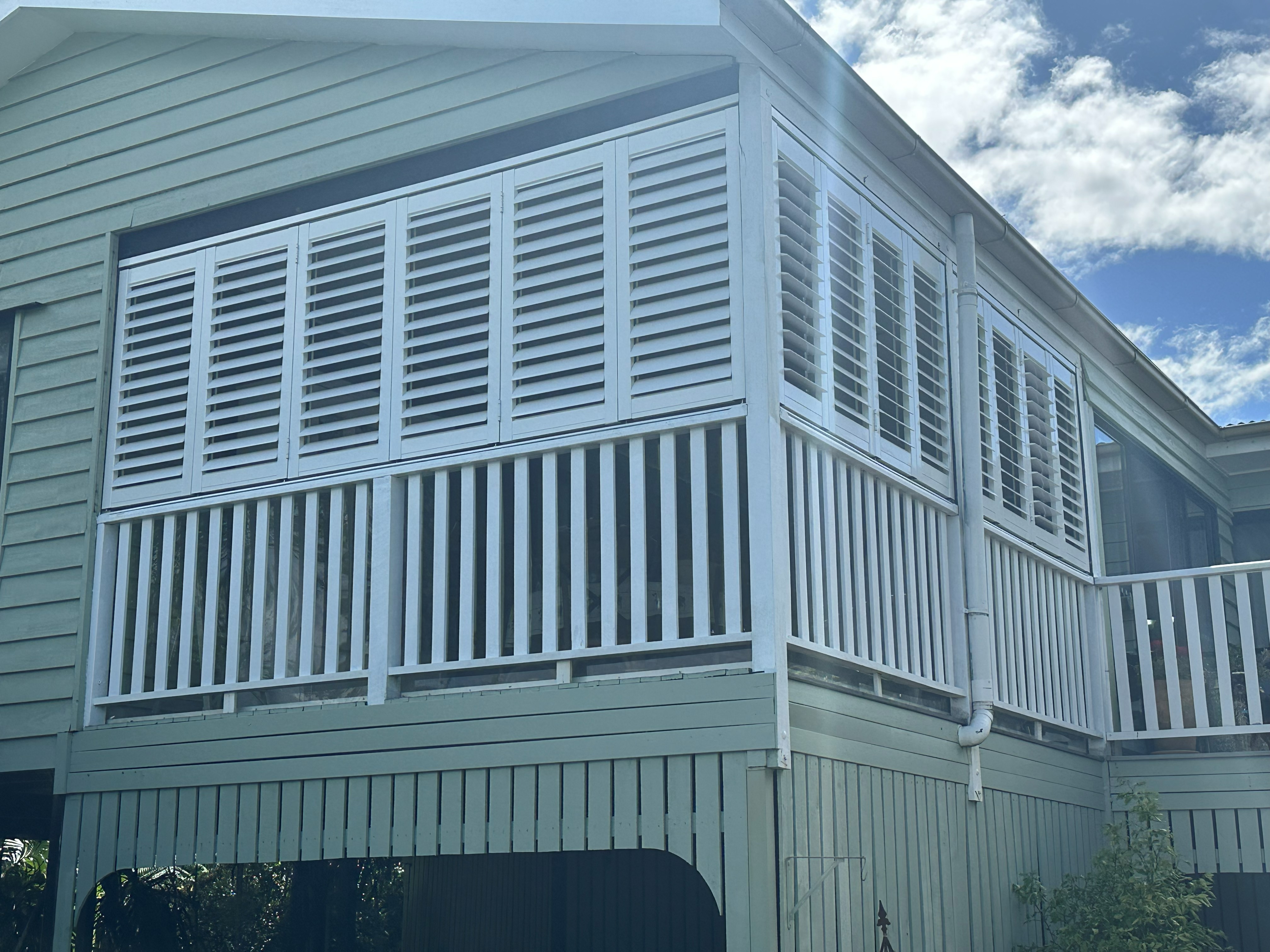 White aluminium shutters fitted around the corner of a Queenslander-style home