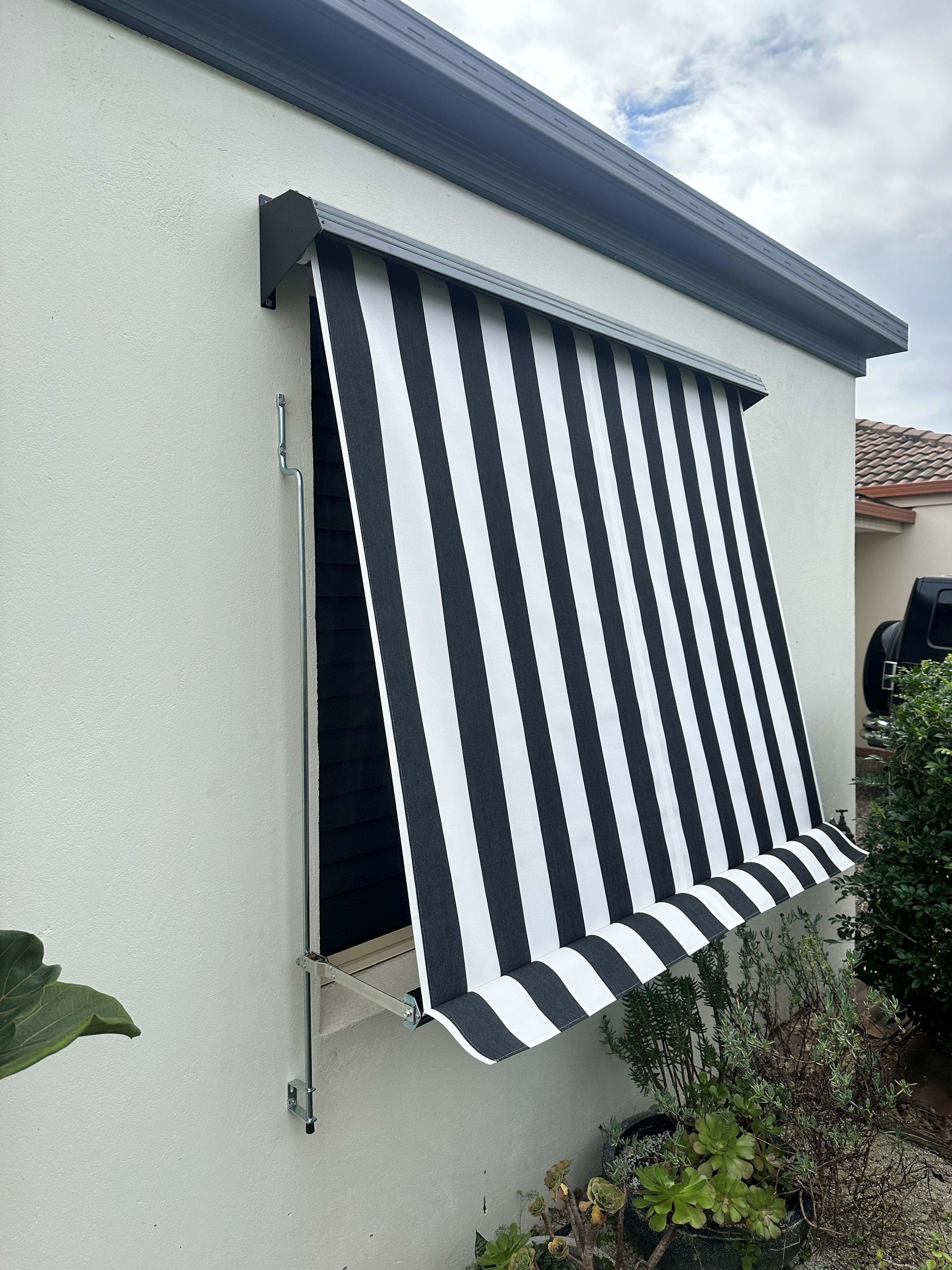 Auto guide awning fully lowered on a balcony with striped fabric