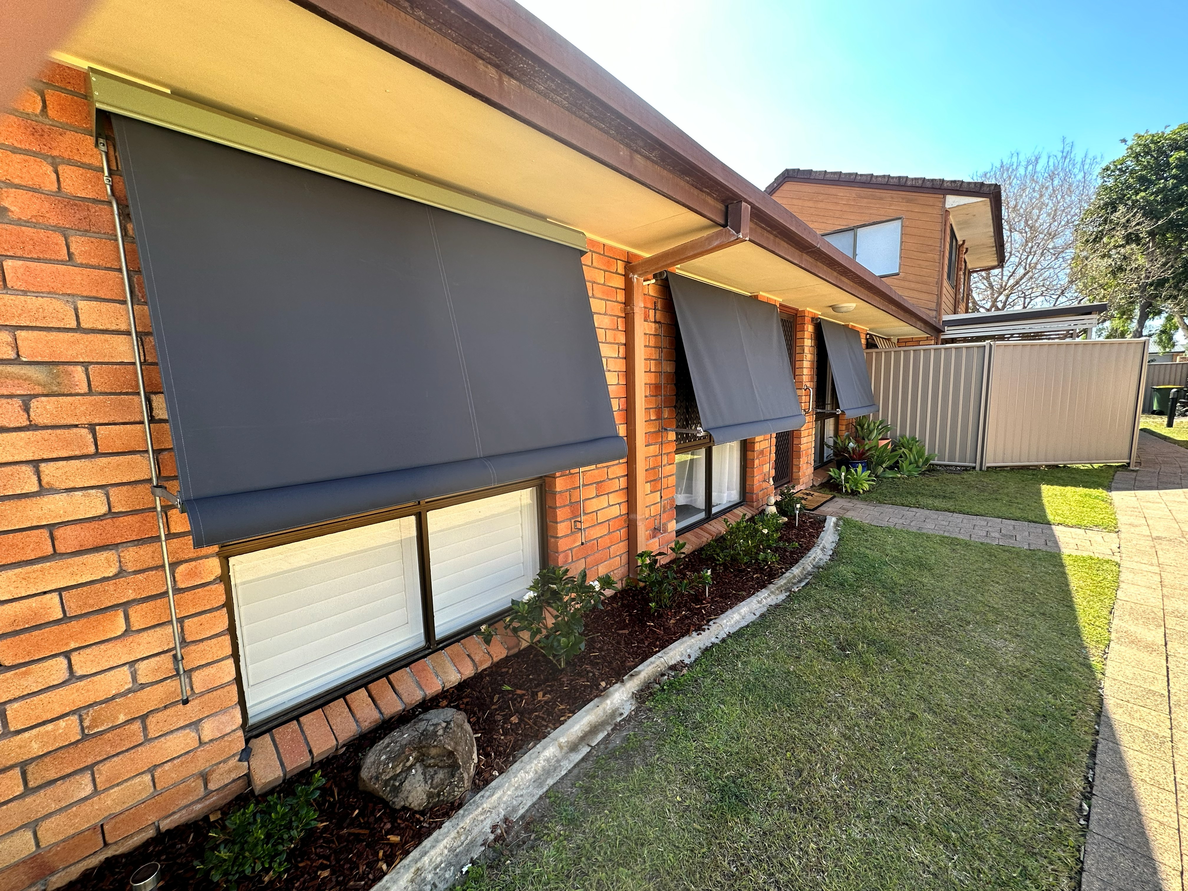 Dark grey auto guide awnings fitted along a brick home exterior