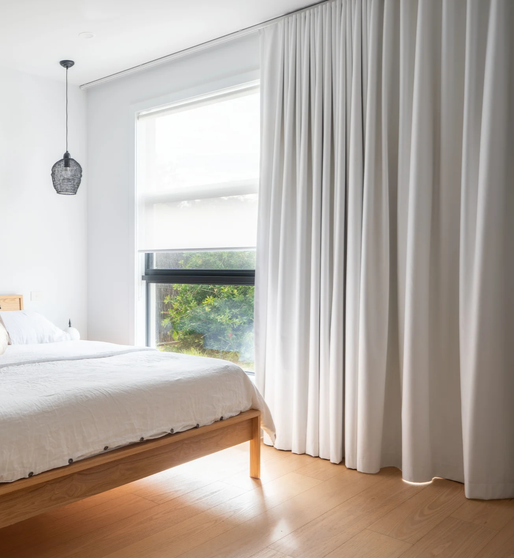 White block out curtains beside a bedroom window with a garden view
