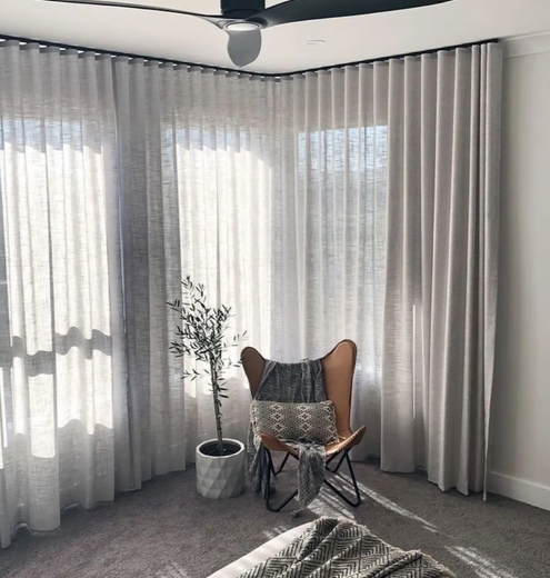 Curved track curtains fitted around a bay window corner beside an armchair