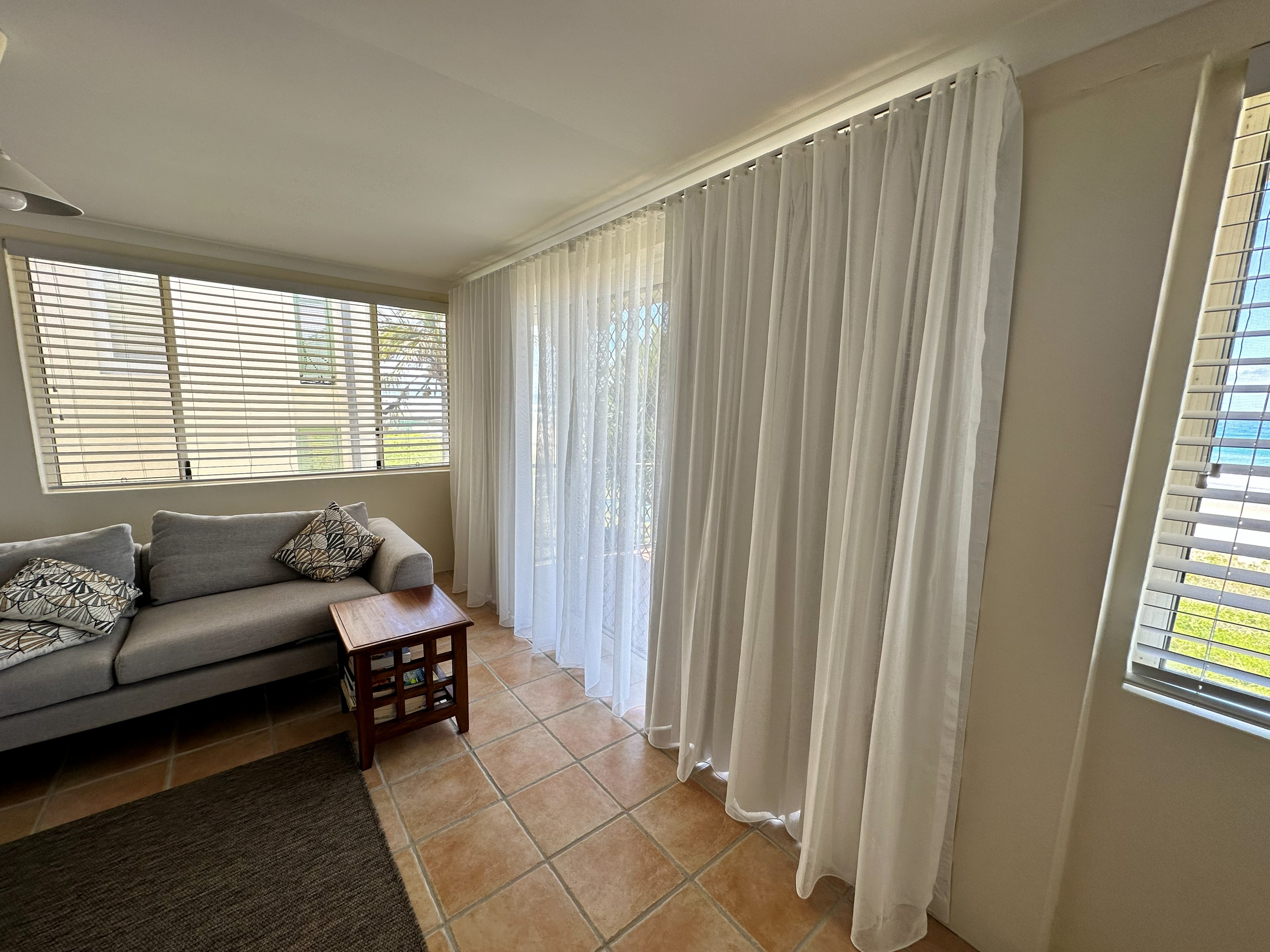 Double track curtains with sheer and blockout layers beside a beachfront sofa