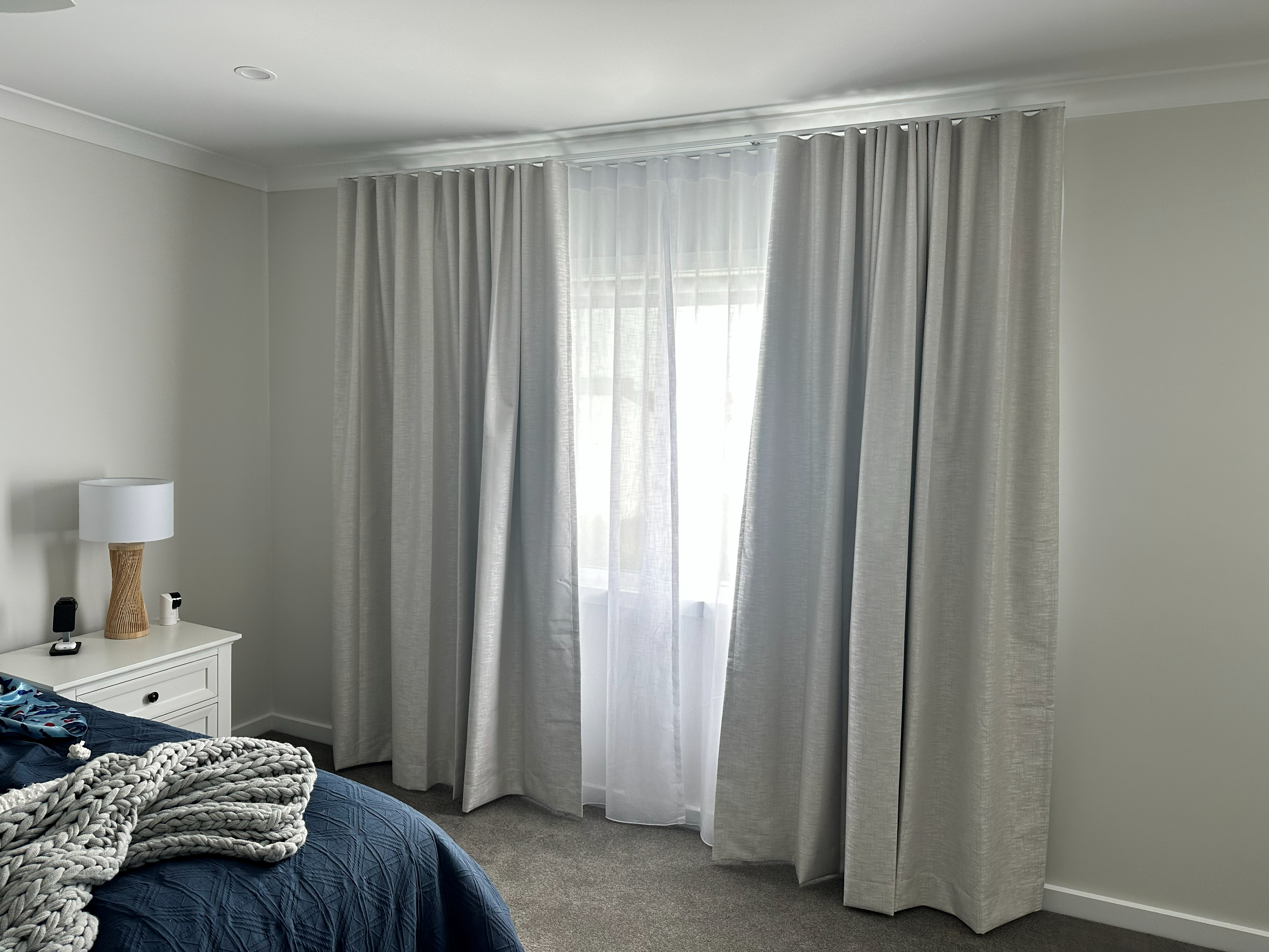 Double track curtains with sheer and blockout layers in a bedroom beside a nightstand