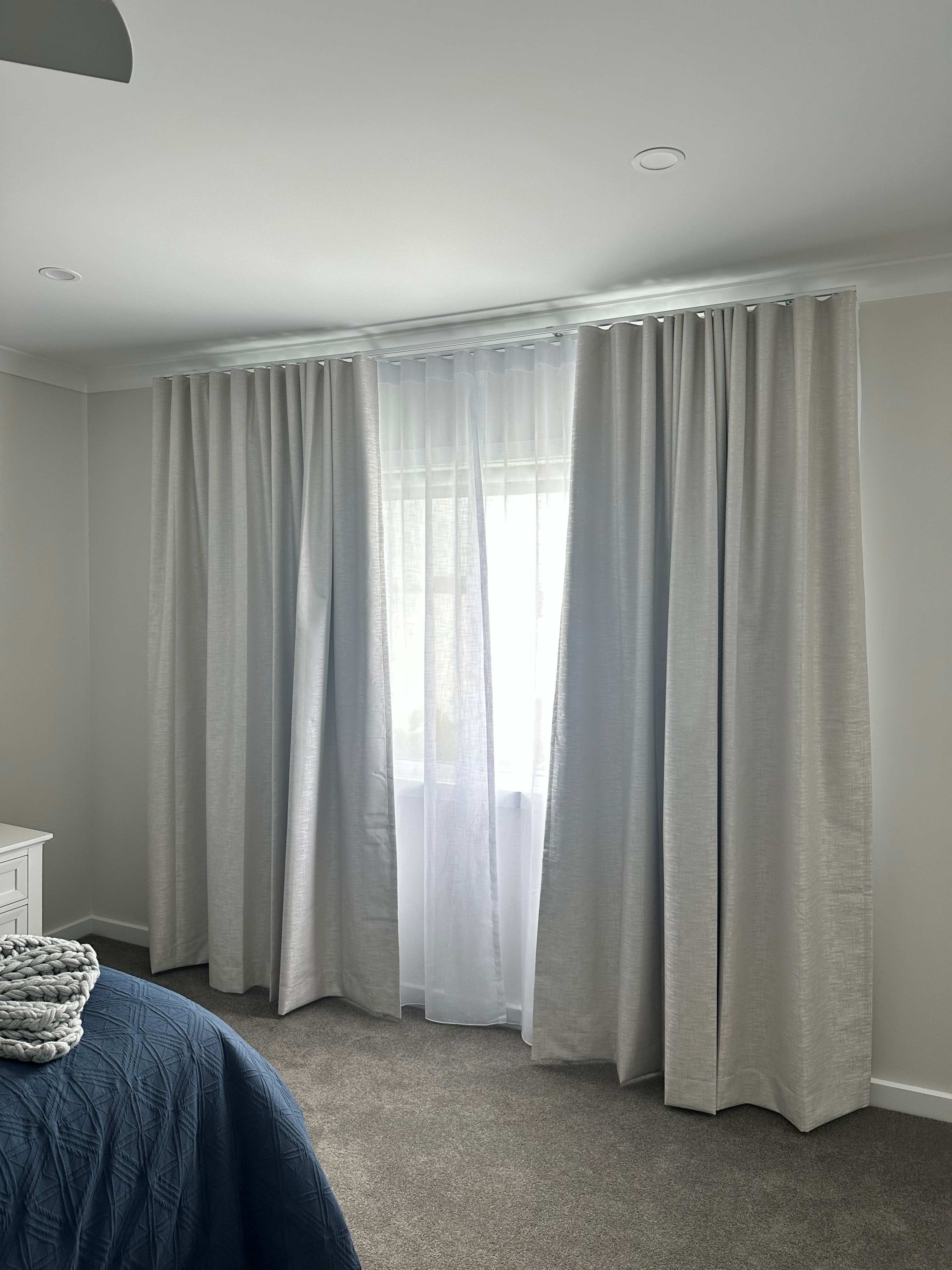 Double track curtains with sheer and blockout layers in a bedroom beside a knitted throw