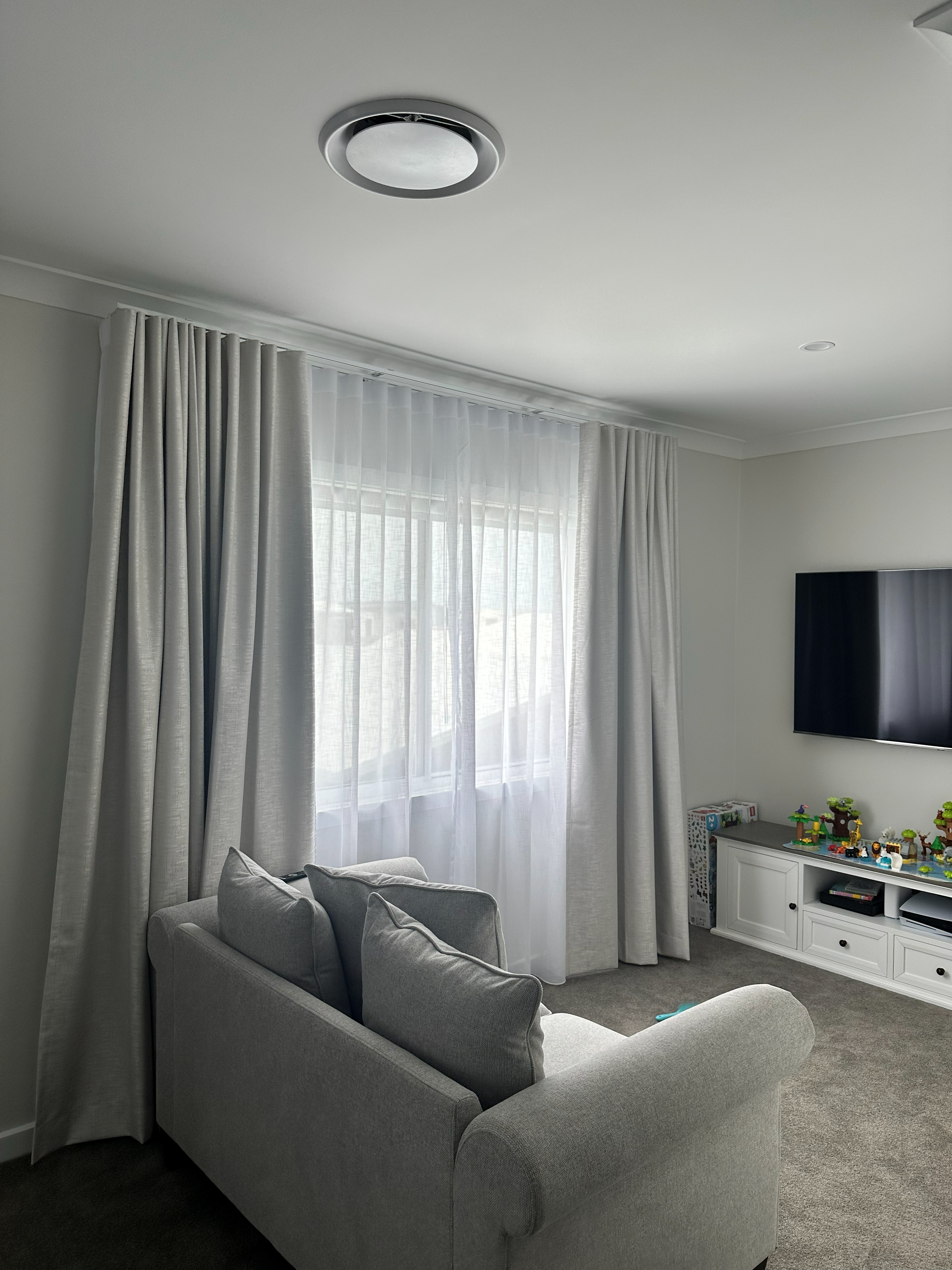 Double track curtains with sheer and blockout layers in a living room beside a wall-mounted TV