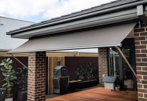 Grey drop arm awning extended over a brick home patio