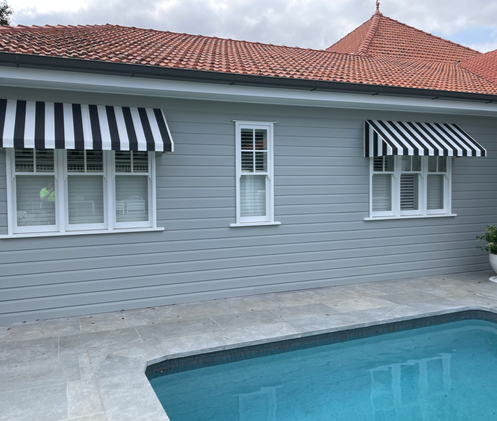 Striped fixed canopy fabric awnings fitted over windows beside a pool