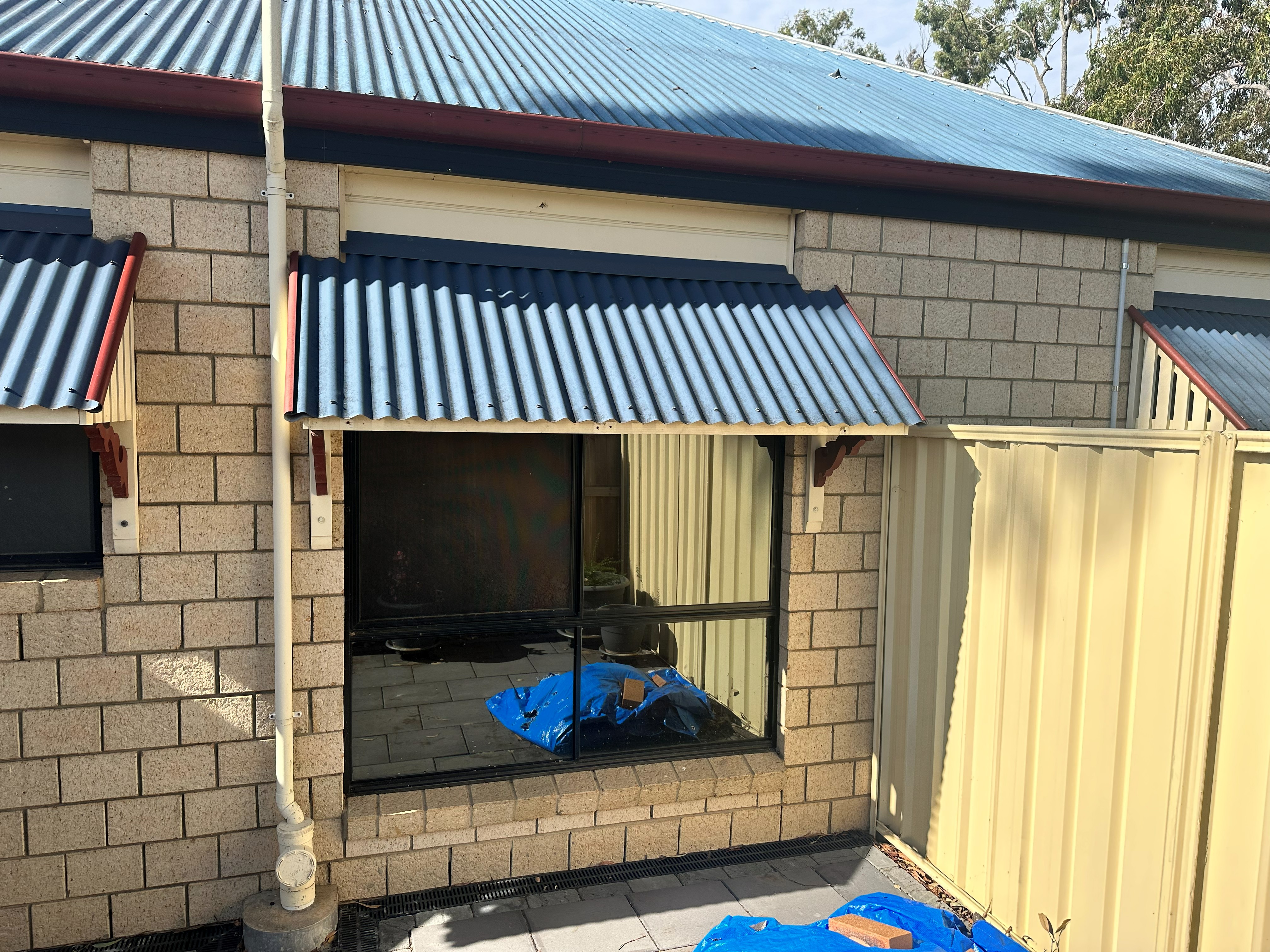 Corrugated metal fixed canopy awning fitted over a brick home window