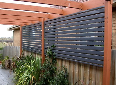 Dark flat fixed privacy screens fitted along a timber pergola above a fence