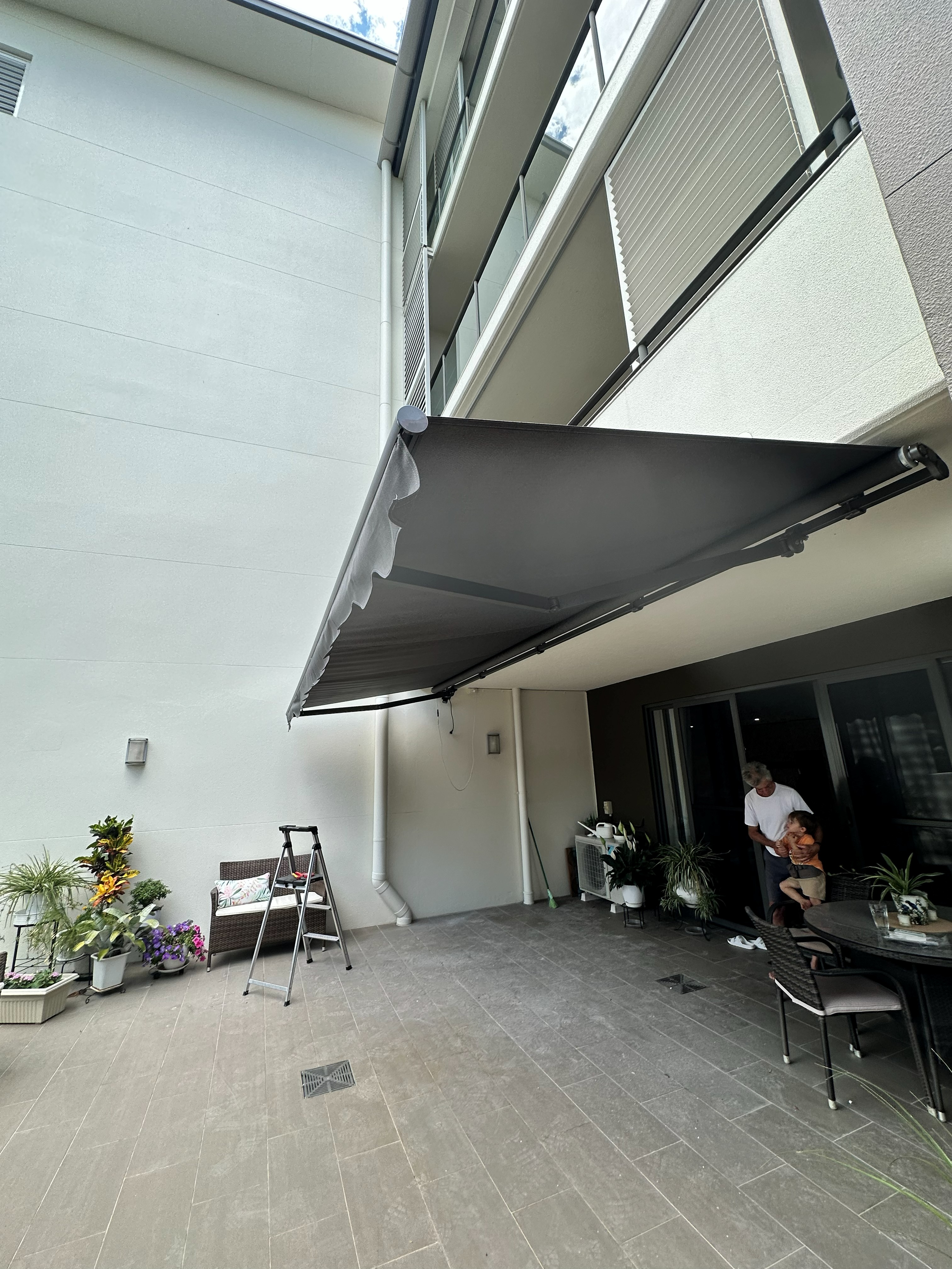 Dark grey folding arm awning extended over a courtyard patio