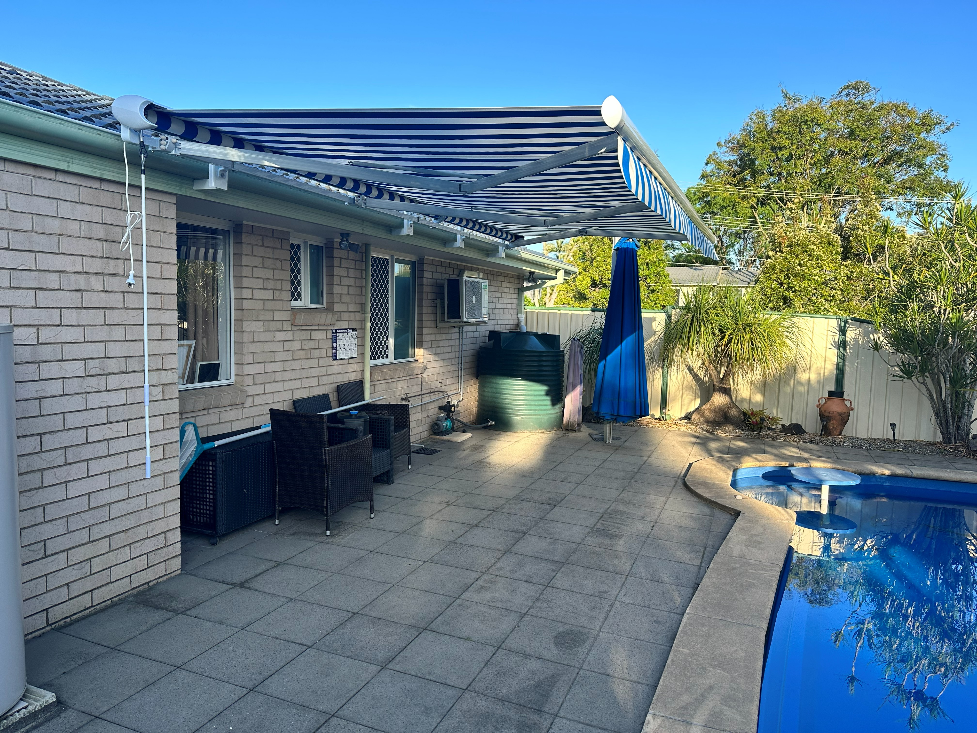 Navy striped folding arm awning extended over a poolside patio