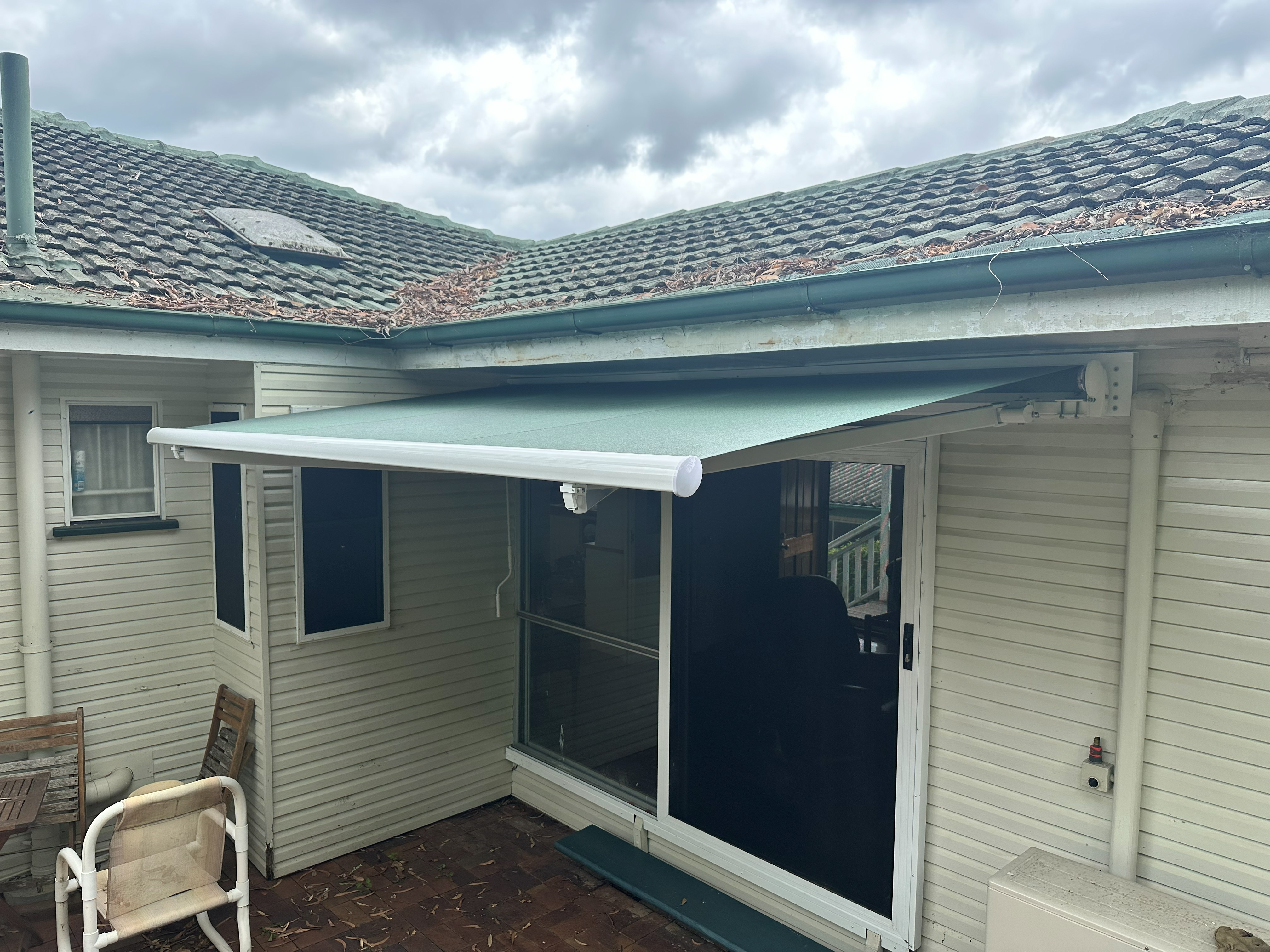 Green folding arm awning extended over a courtyard entrance