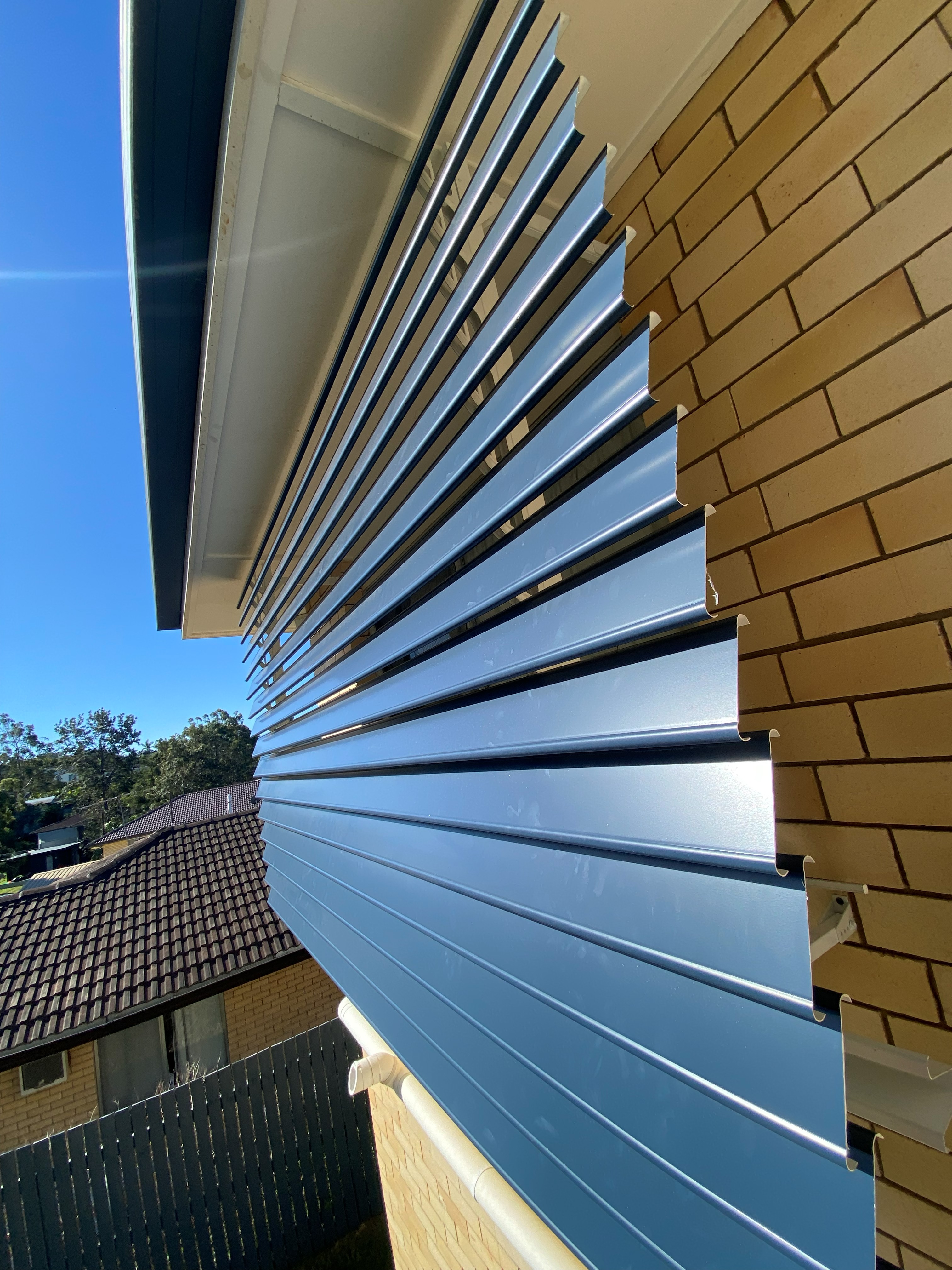 Close-up of a blue-grey aluminium louvre awning fitted to a brick home
