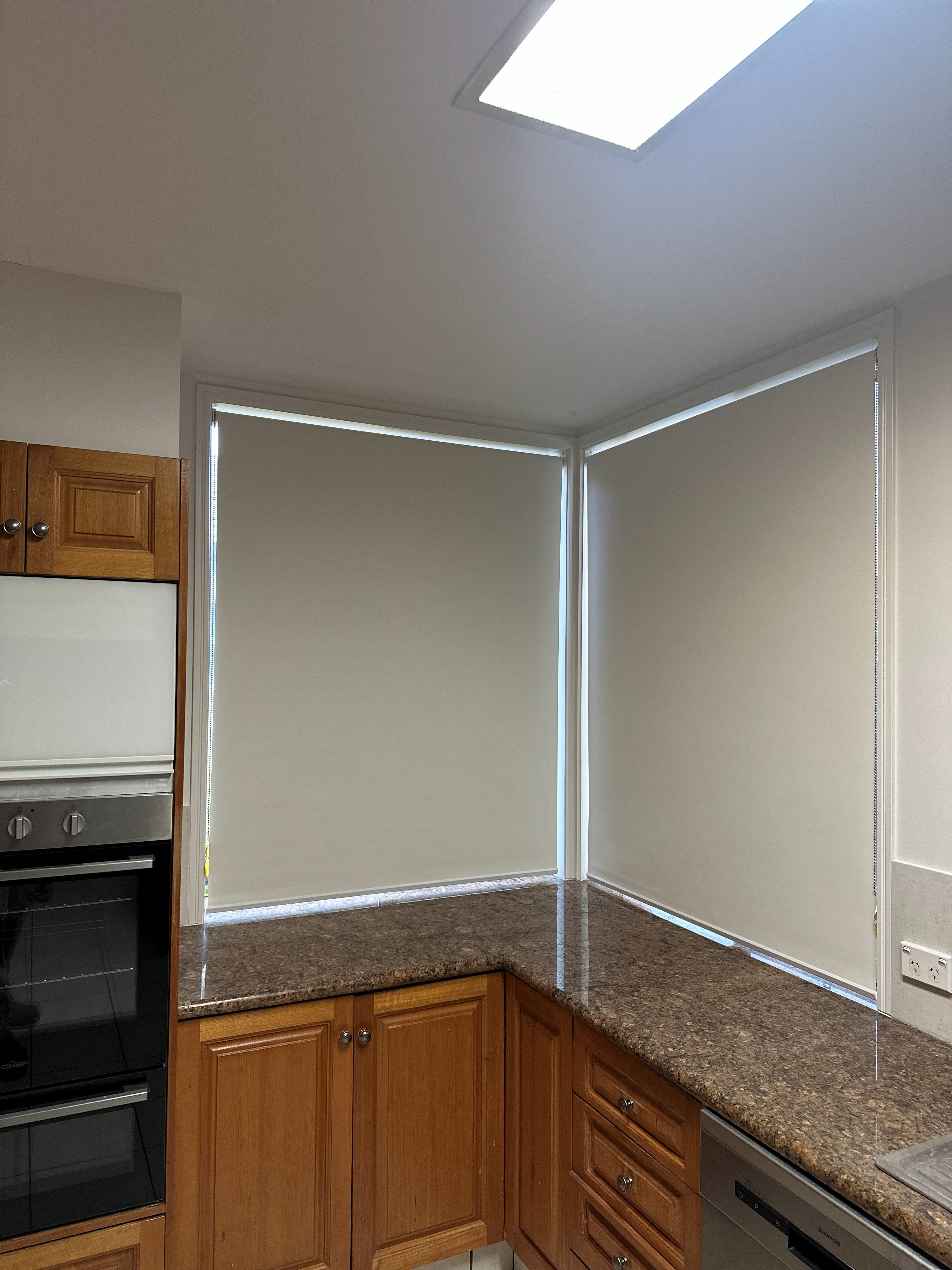 Grey roller blinds fitted to a corner kitchen window above the sink