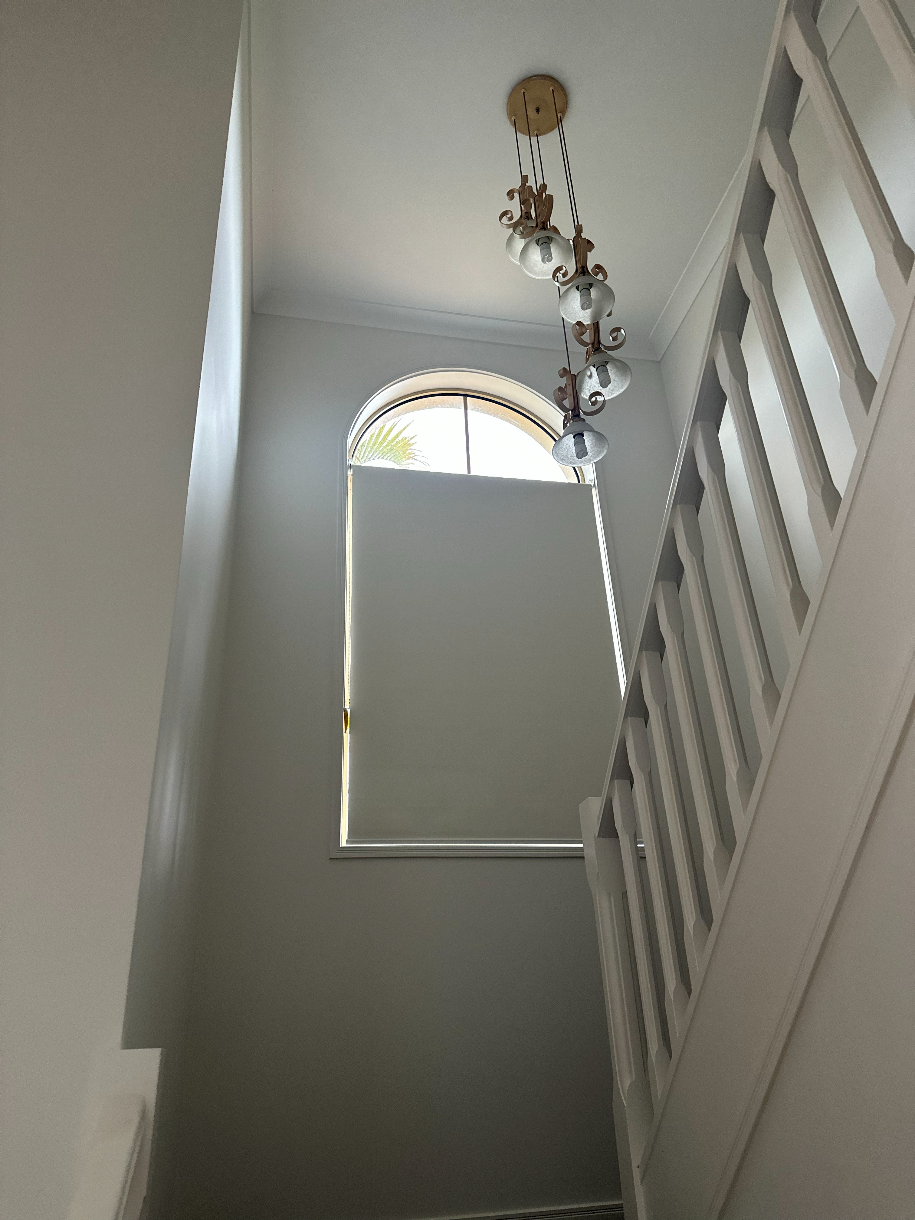 Grey roller blind over an arched stairwell window