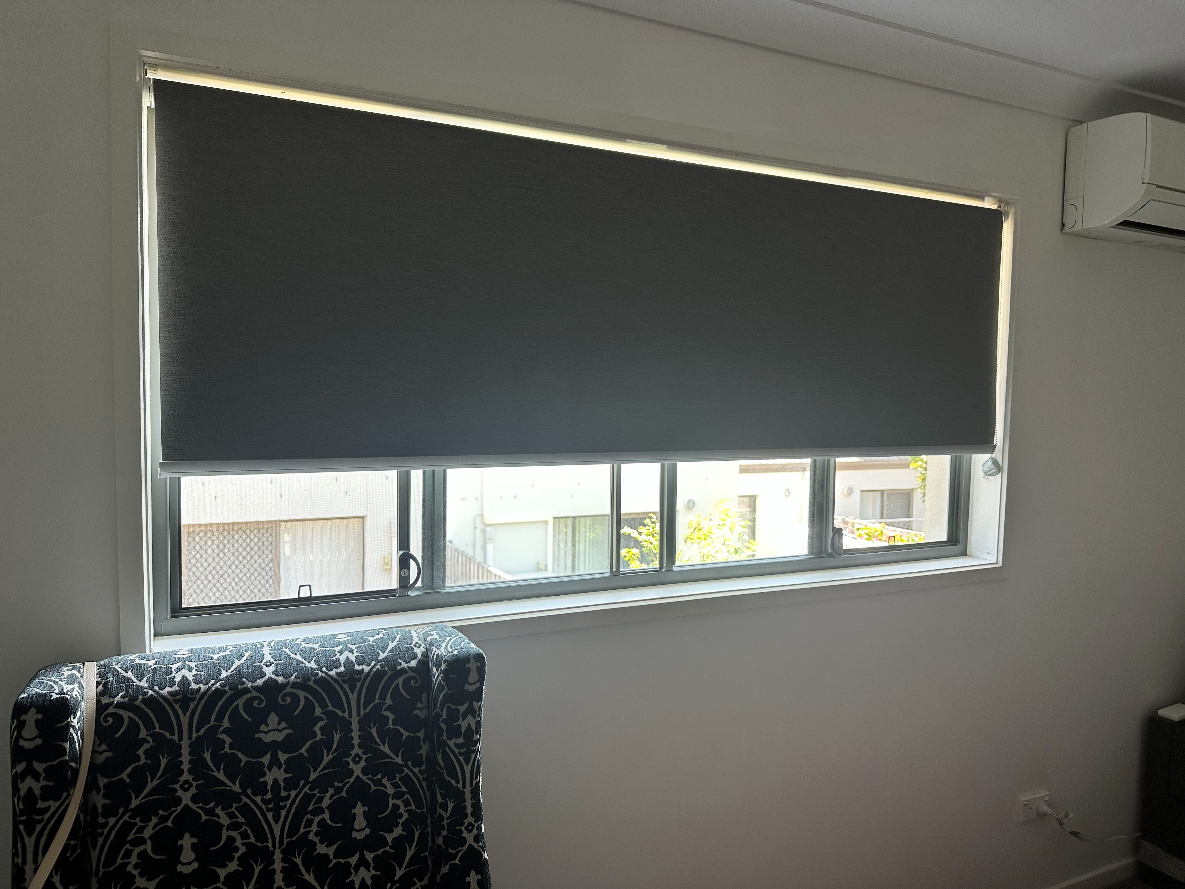 Dark grey roller blind over a wide living room window