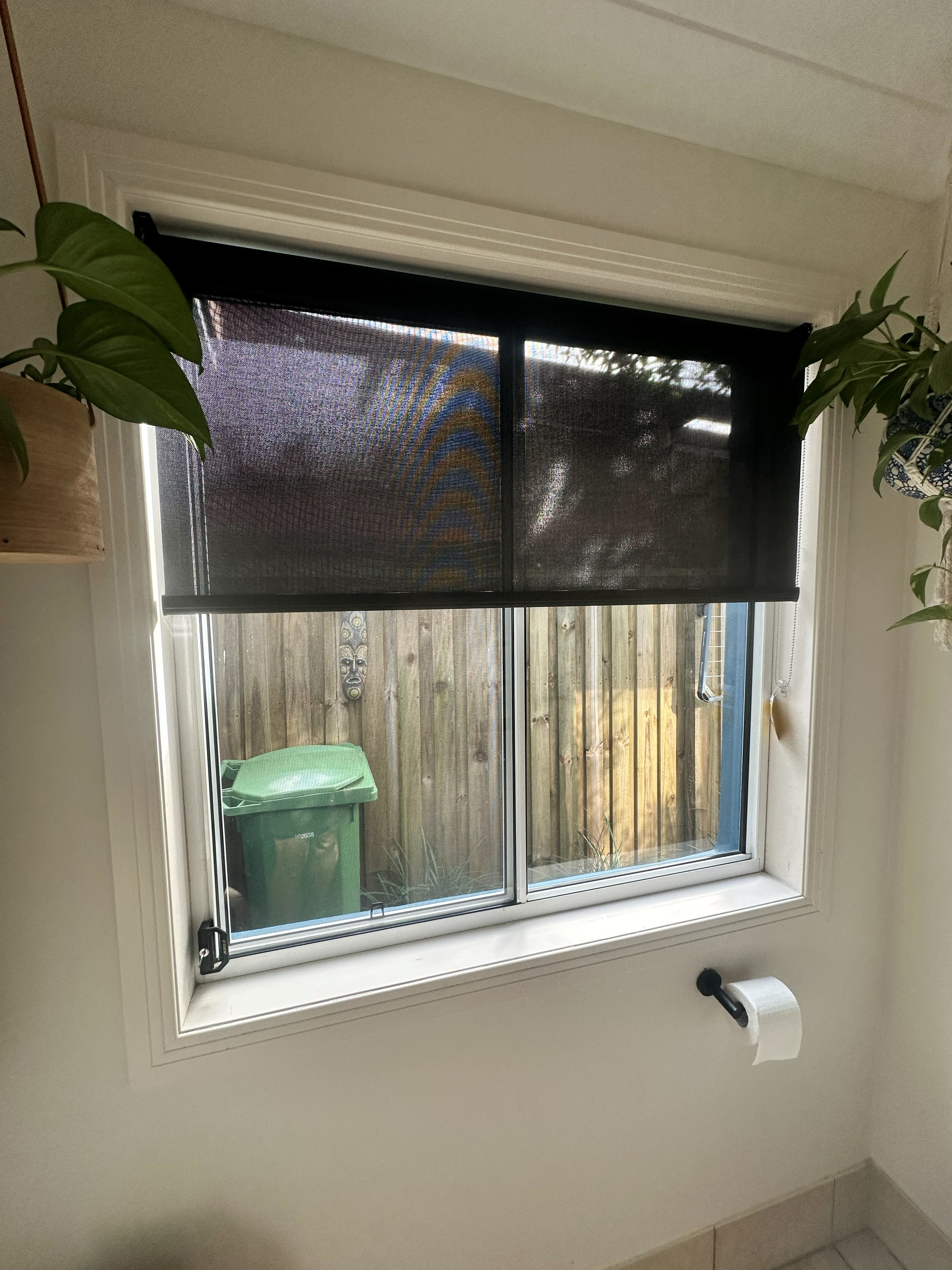 Black sunscreen roller blind lowered over a bathroom window