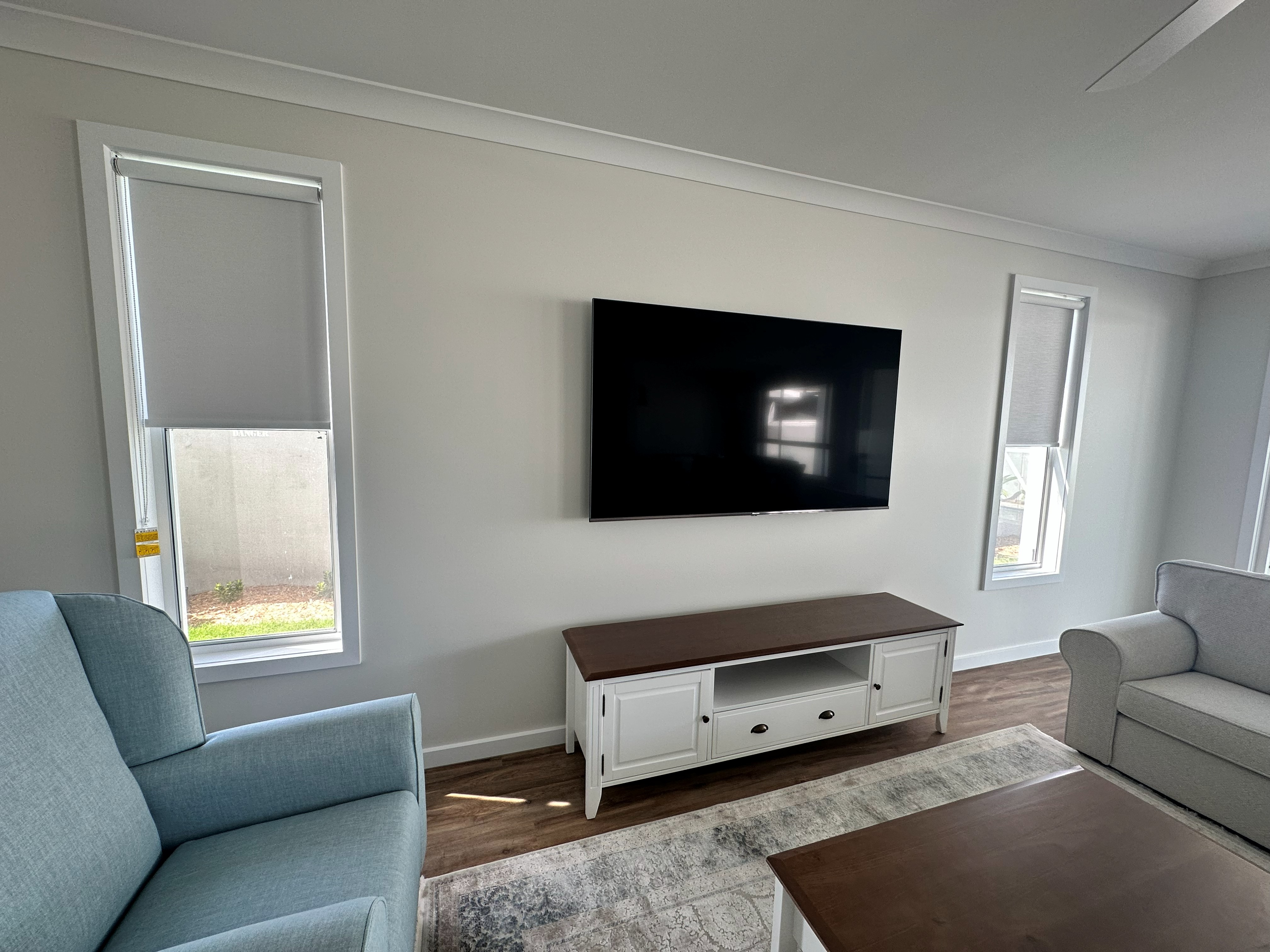 Grey roller blinds fitted to living room windows either side of a TV wall