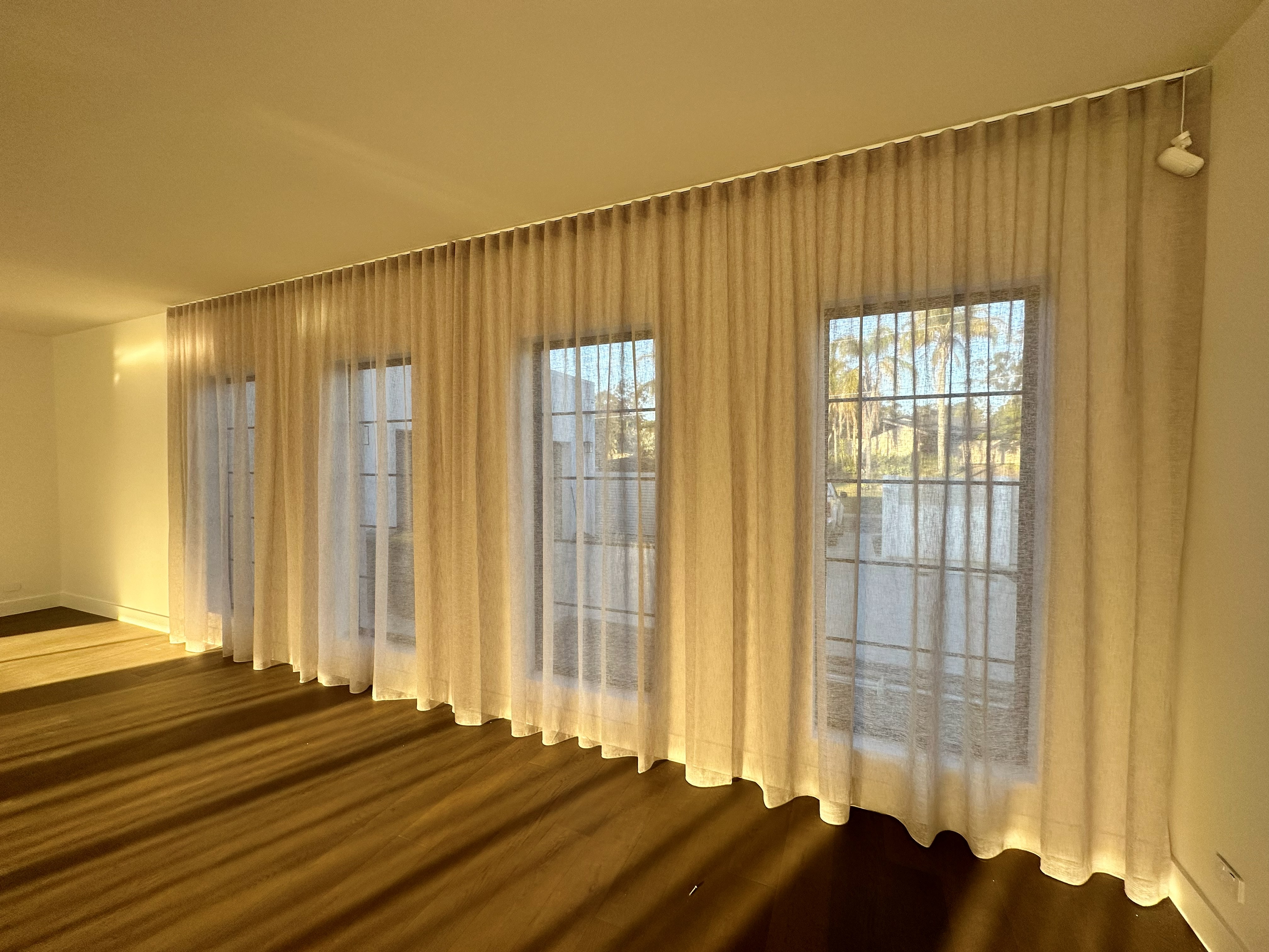 Sheer curtains fitted across multiple windows in a living room at golden hour