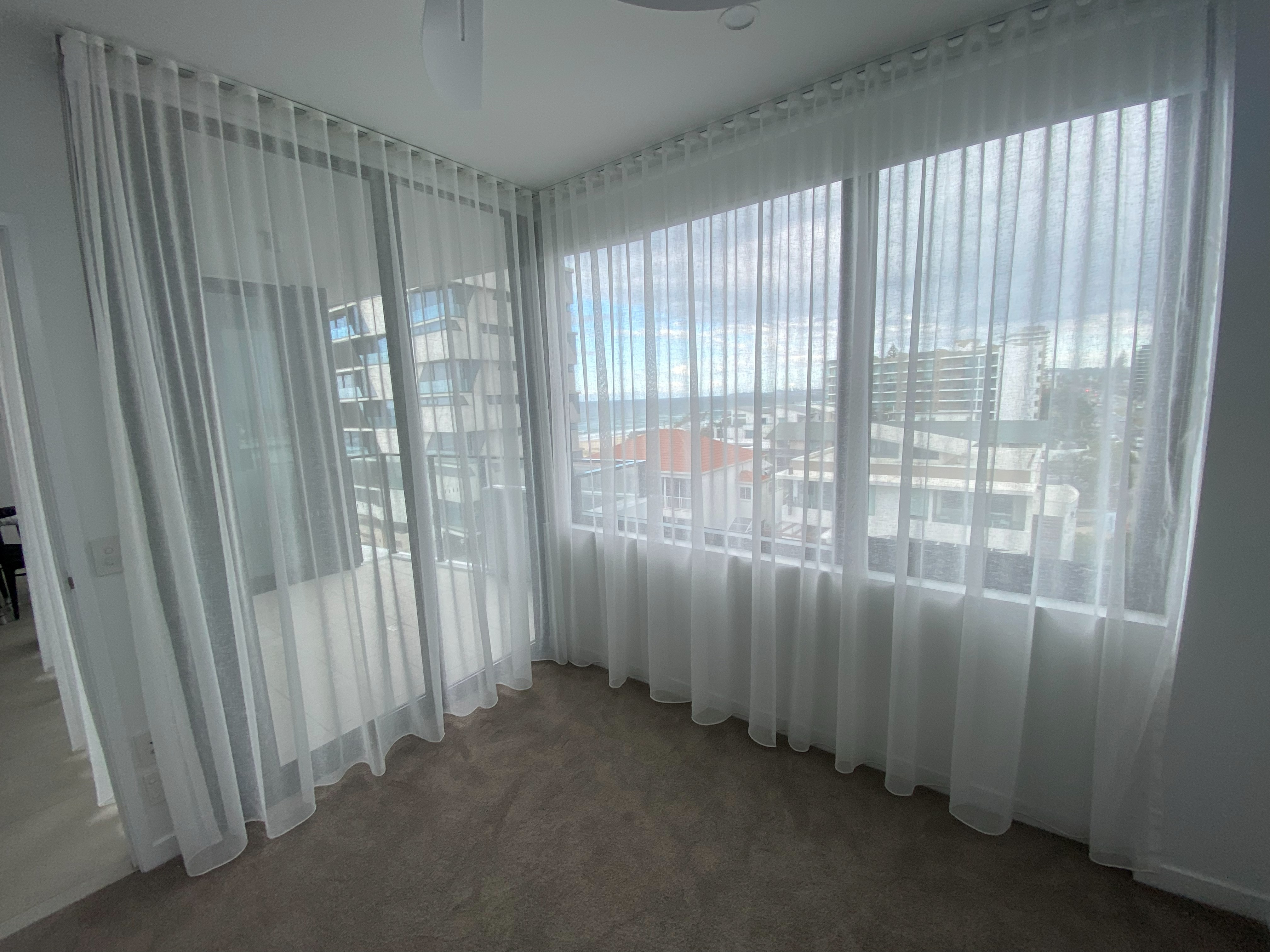 Sheer curtains in a corner living room overlooking a coastal high-rise view