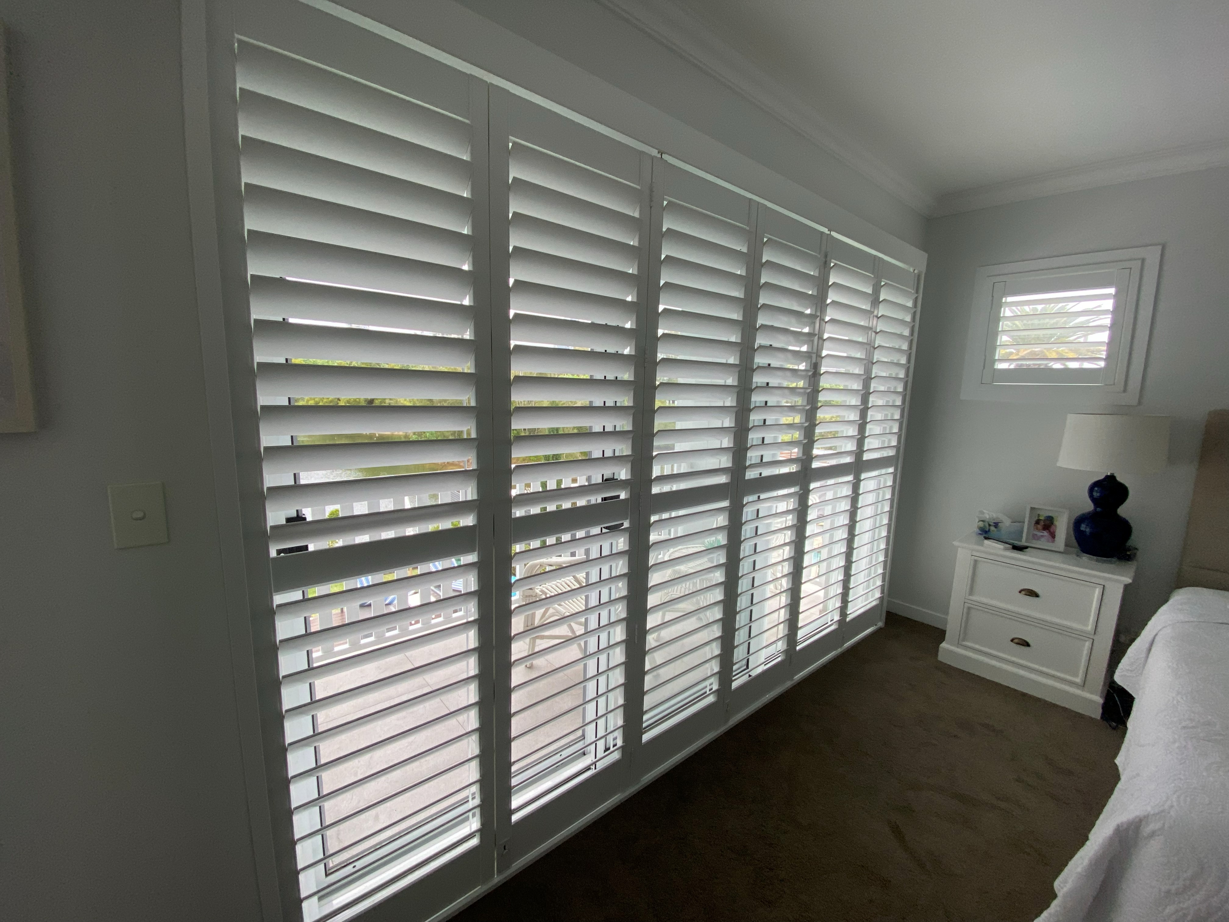Six-panel plantation shutter window in a bedroom overlooking a pool