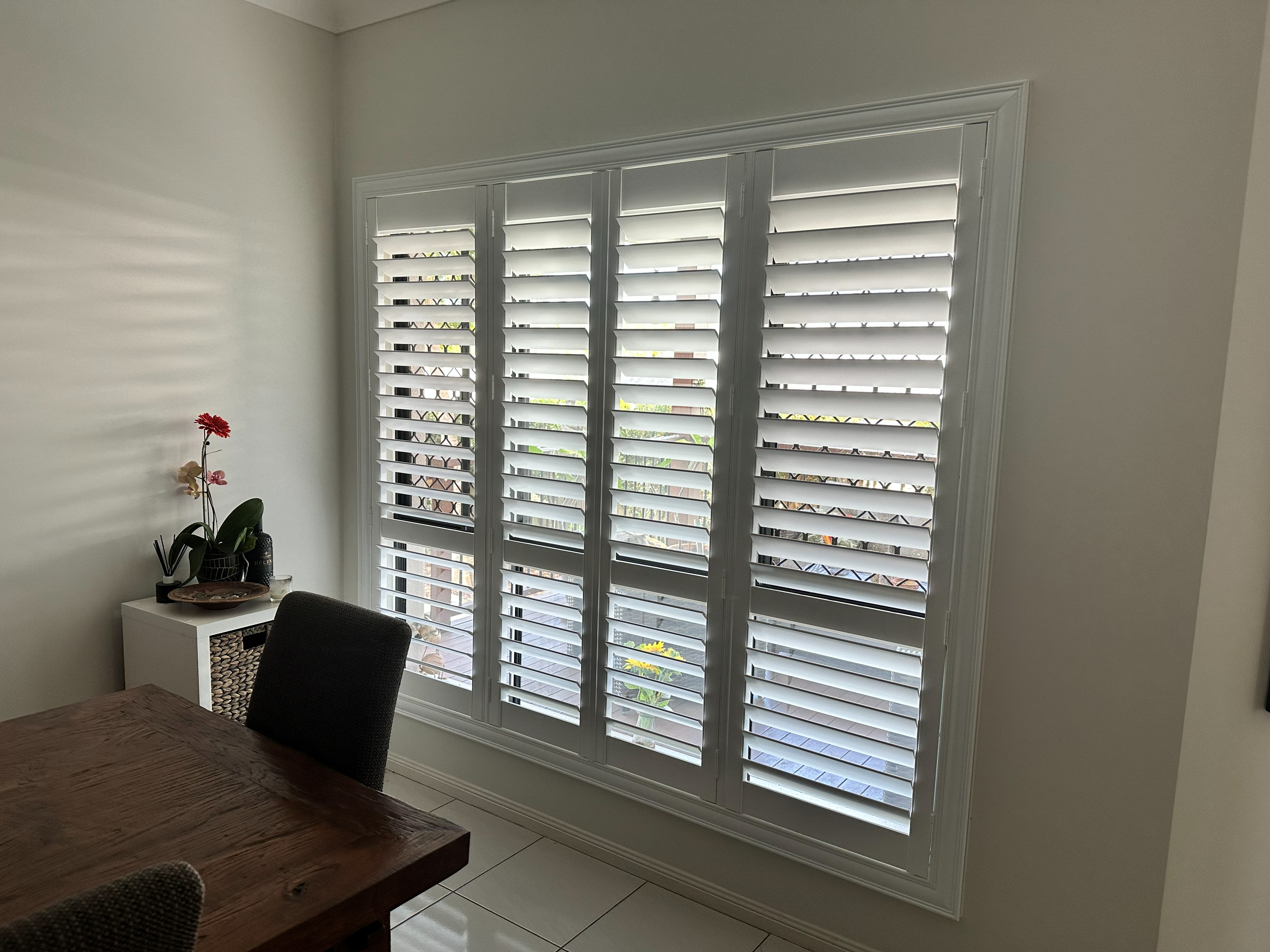 Plantation shutters in a dining room with a timber table and flowers