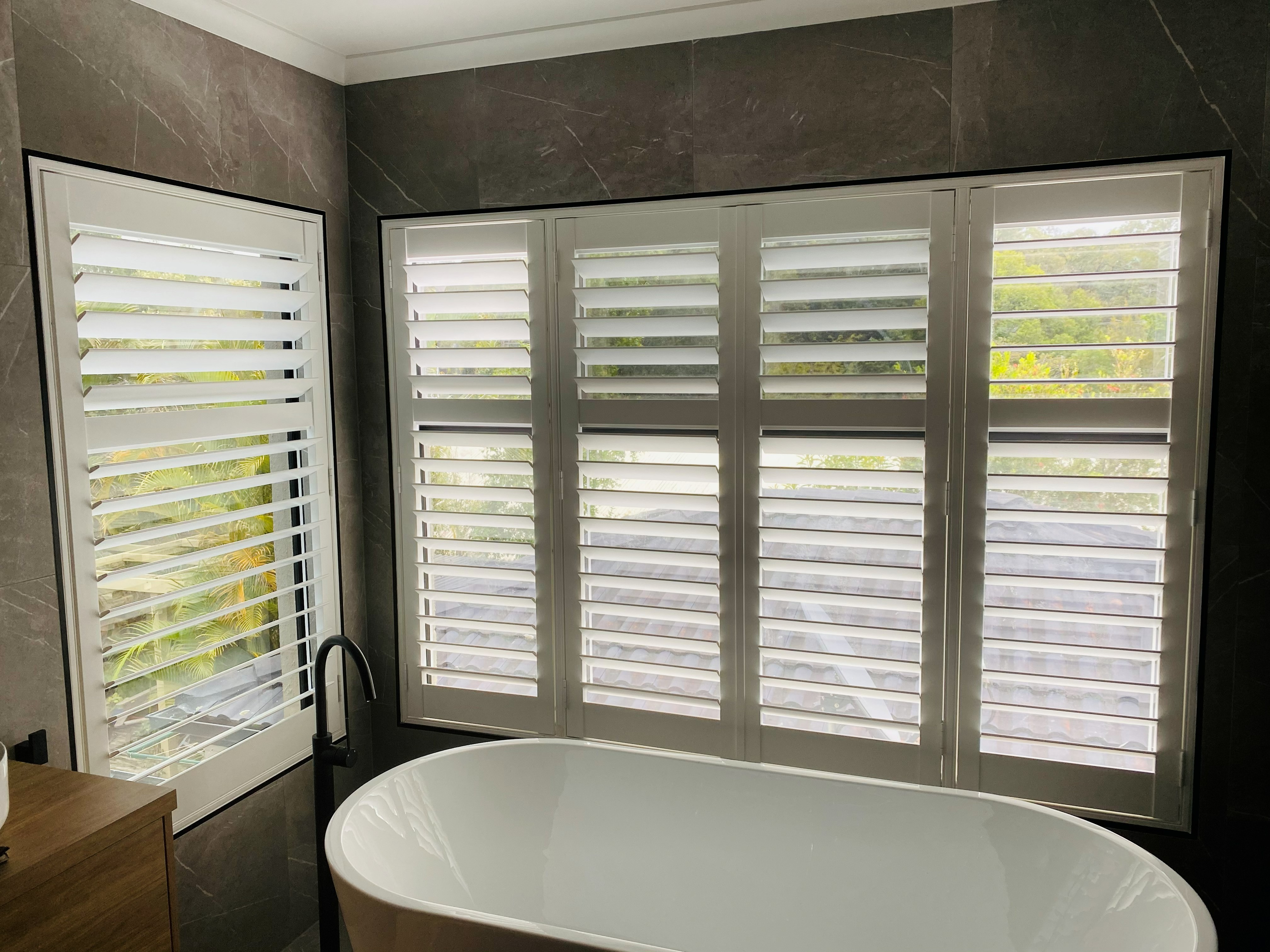 Plantation shutters in a dark marble bathroom with a freestanding bathtub