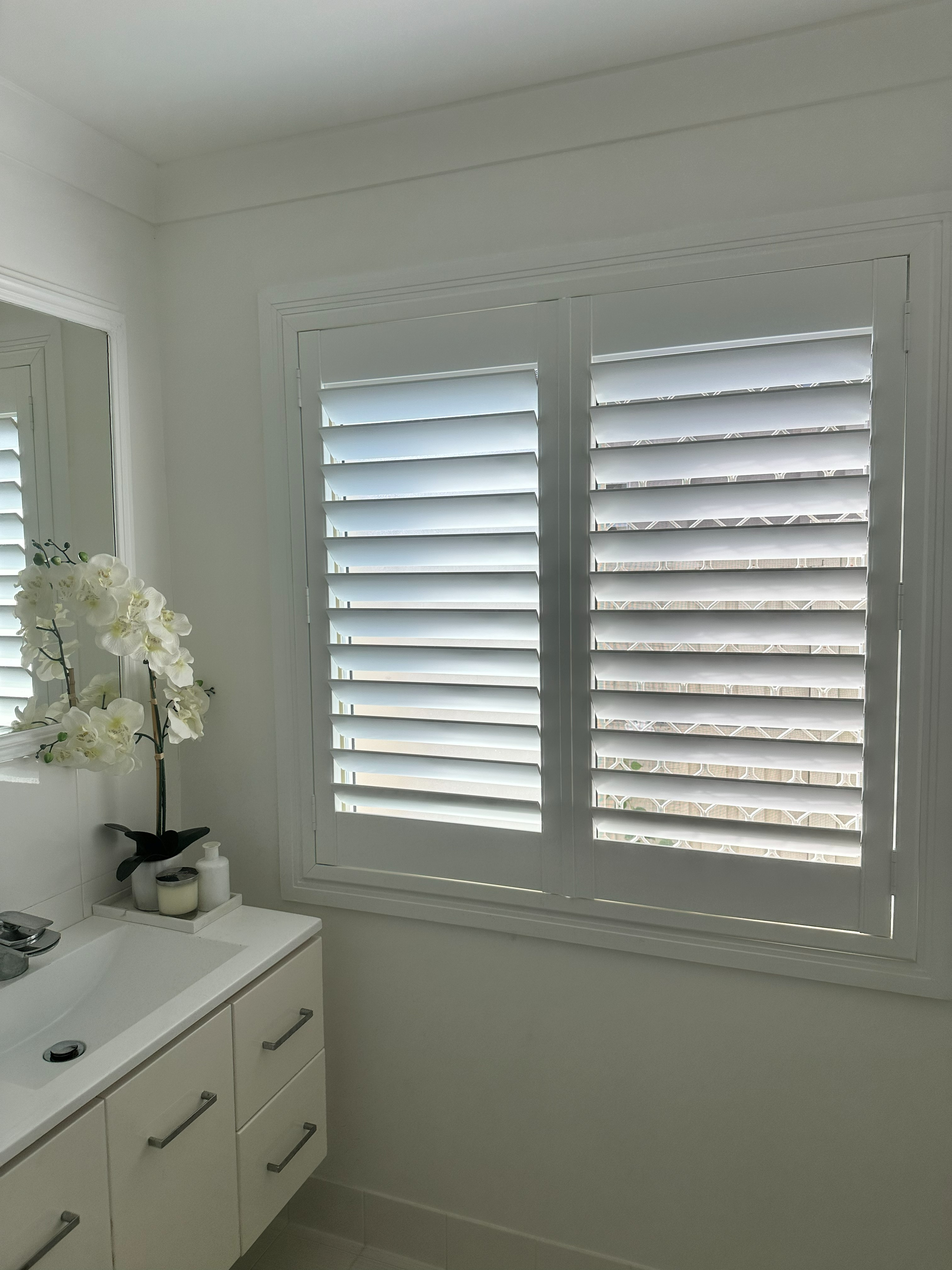 White plantation shutters above a bathroom vanity with orchid flowers