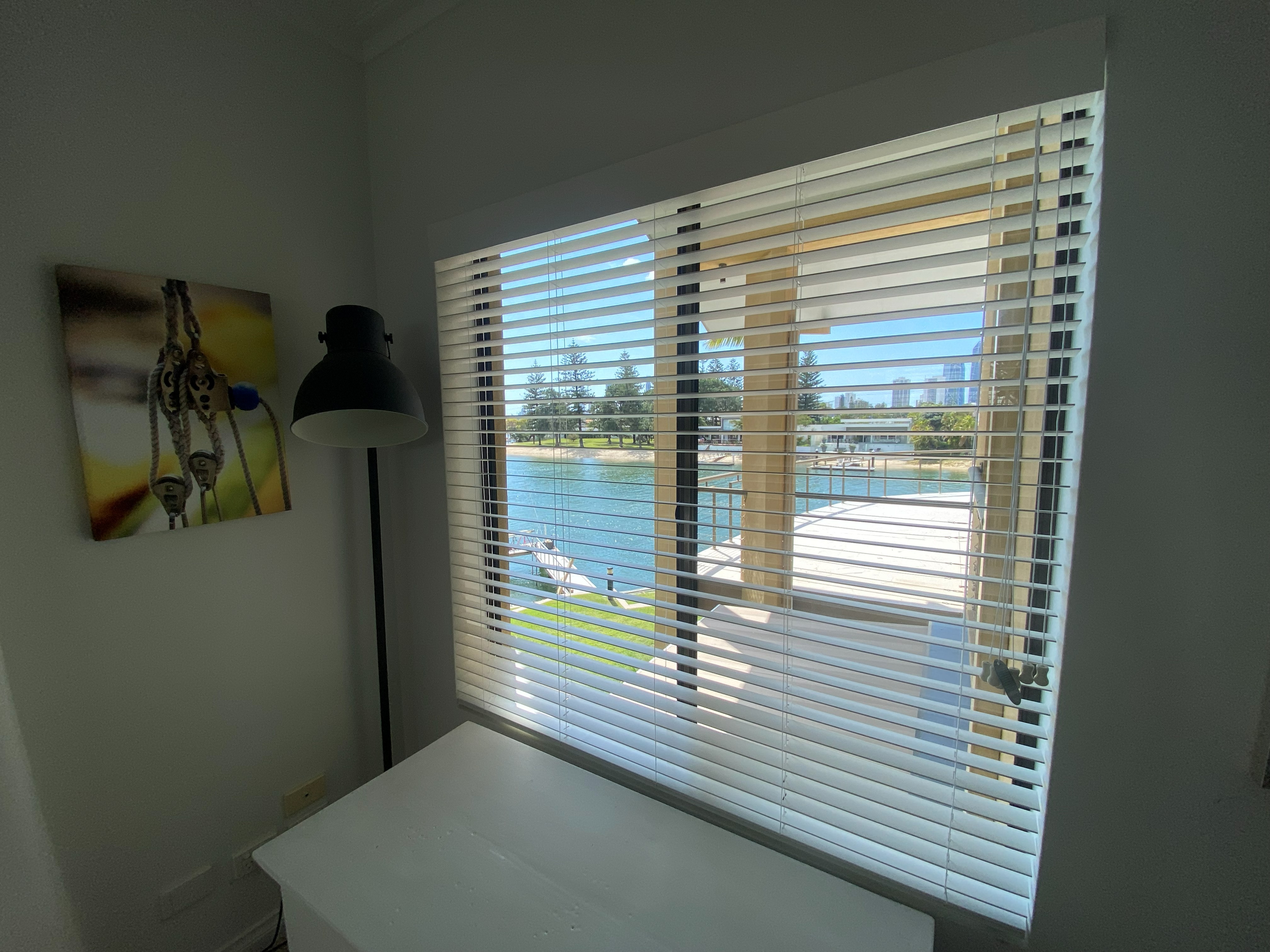 White venetian blinds fitted to a window overlooking a marina and city skyline