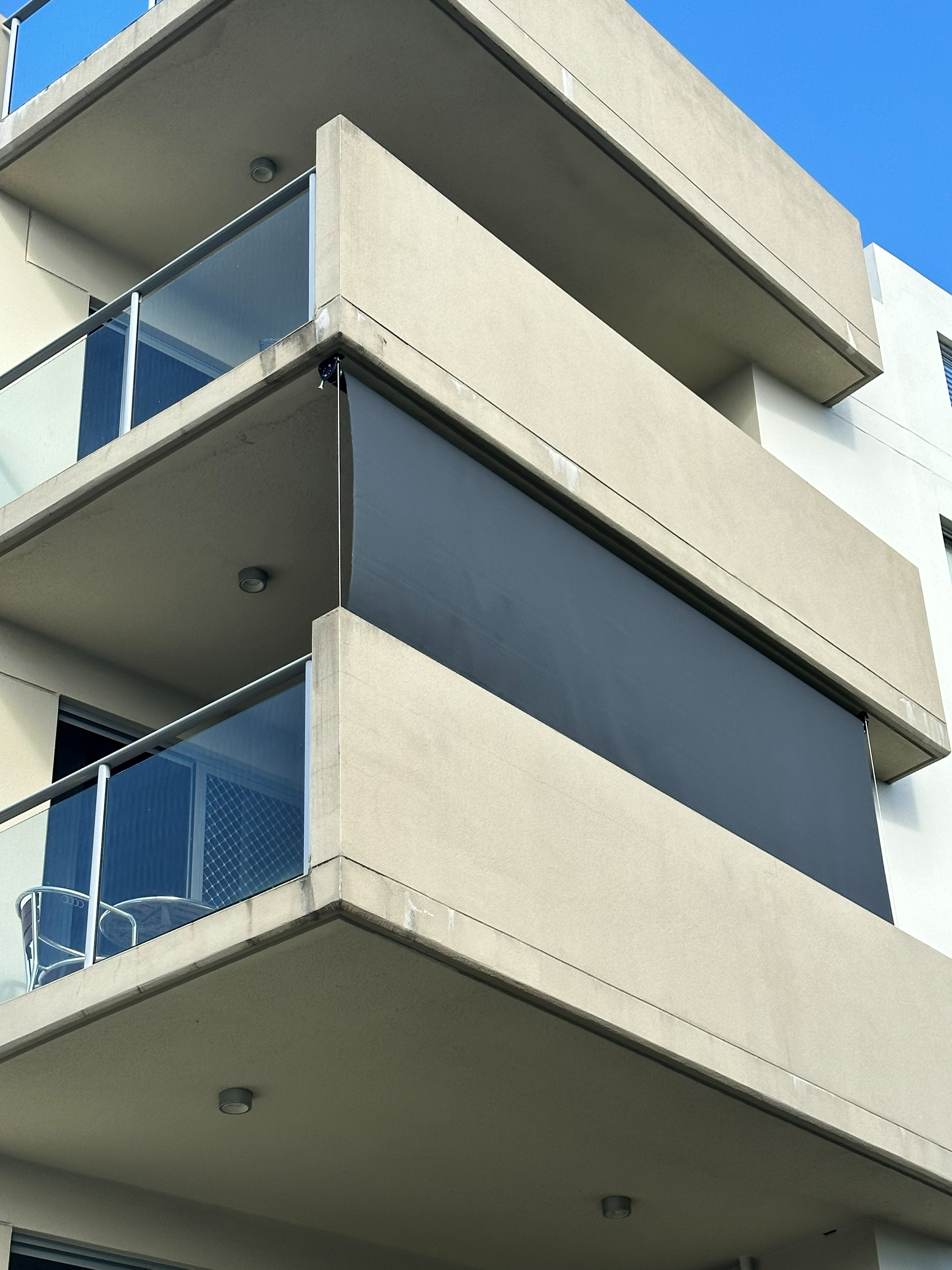 Wire guide outdoor blind fitted to a multi-level balcony corner