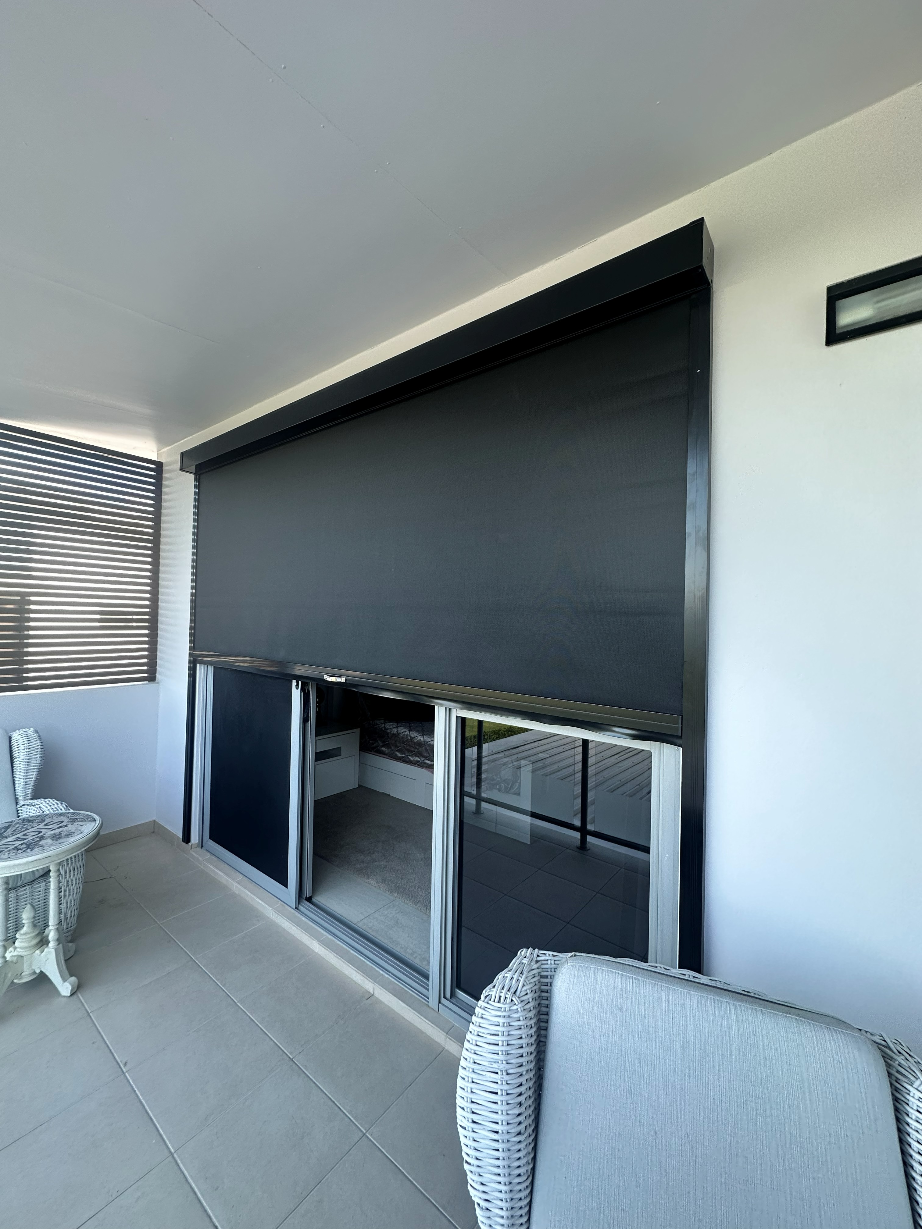 Dark grey Zipscreen fully lowered on a balcony beside sliding doors
