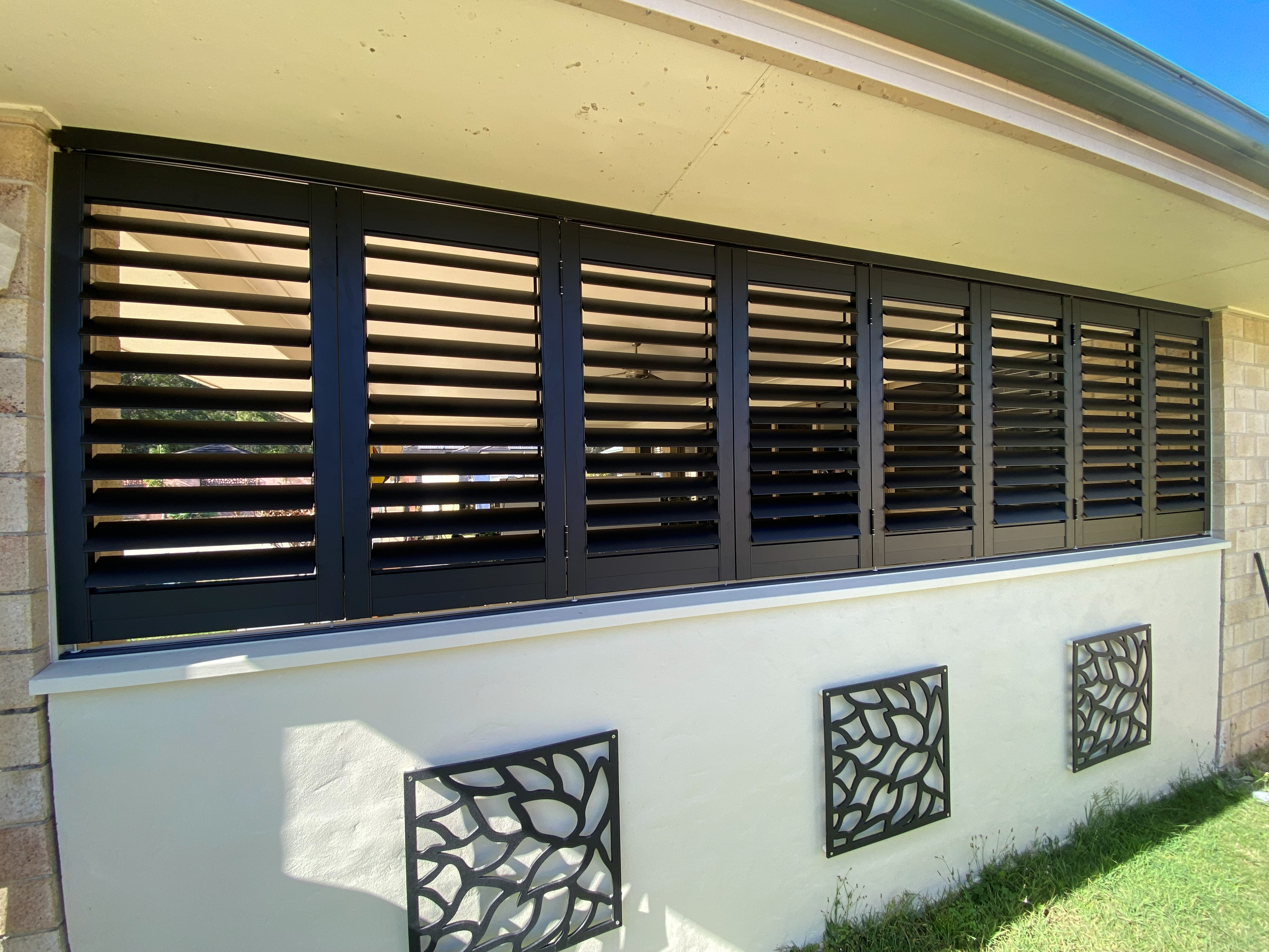 Dark aluminium external shutters installed across a patio window
